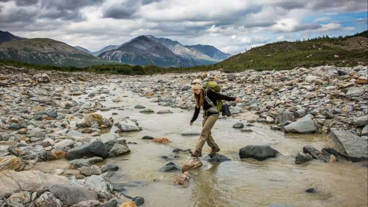 Backpackerin überquert Fluss in abgelegener Bergwildnis, Alaska, USA