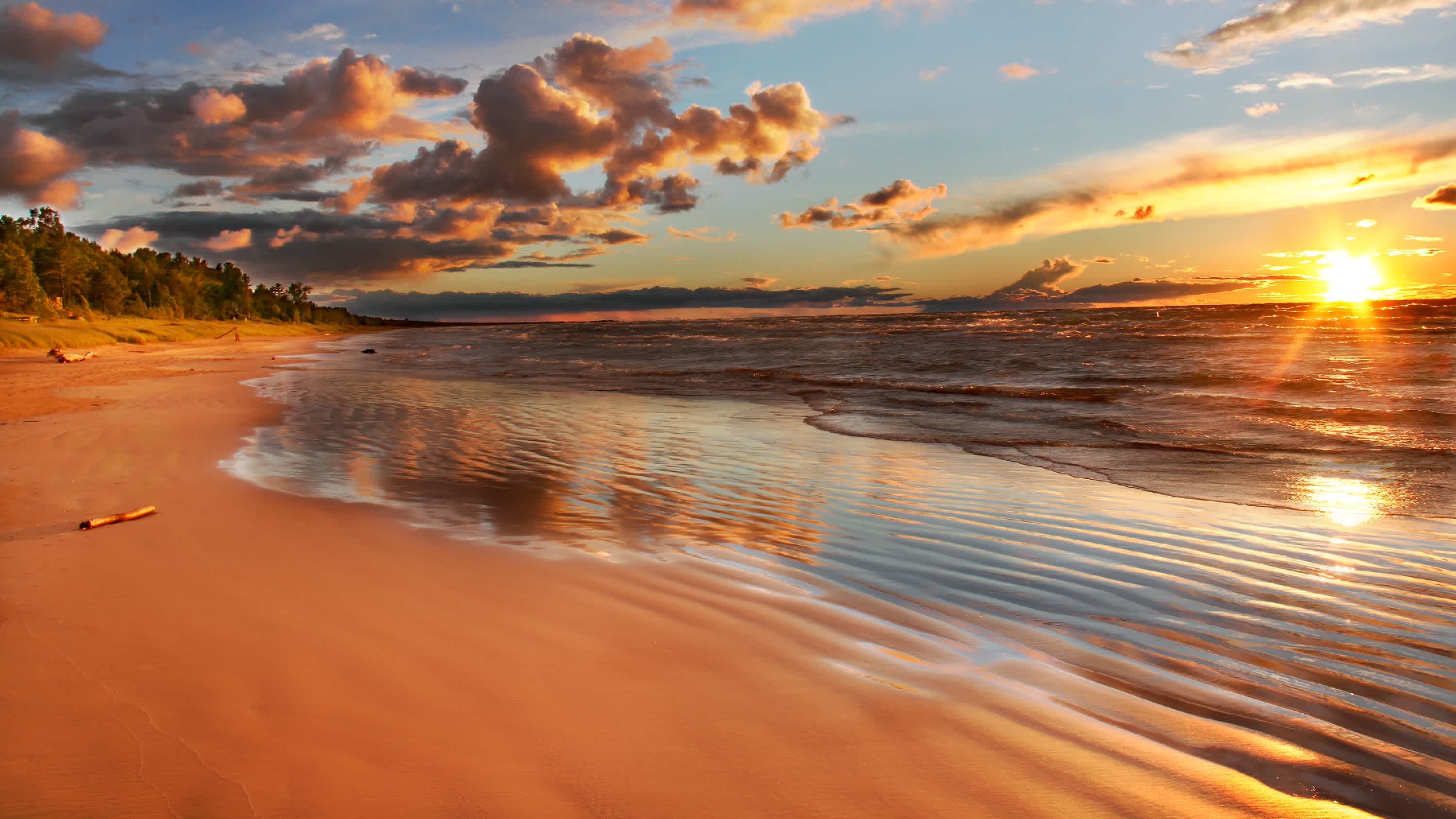 Der malerische Strand Grand Bend Beach am See Lake Huron in Kanada bei orangener Sonnendämmerung und mit farbenprächtigen Wolken und seichtem Wasser.