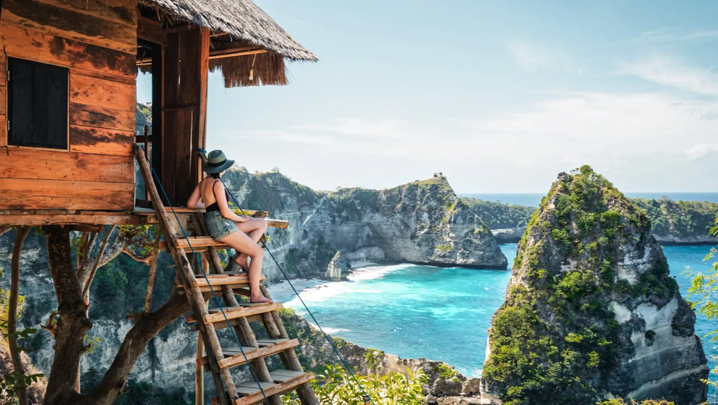 Indonesien Nusa Penida Frau auf Baumhaus mit Blick auf Felsen und Meer, Nusa Penida, Bali, Indonesien.