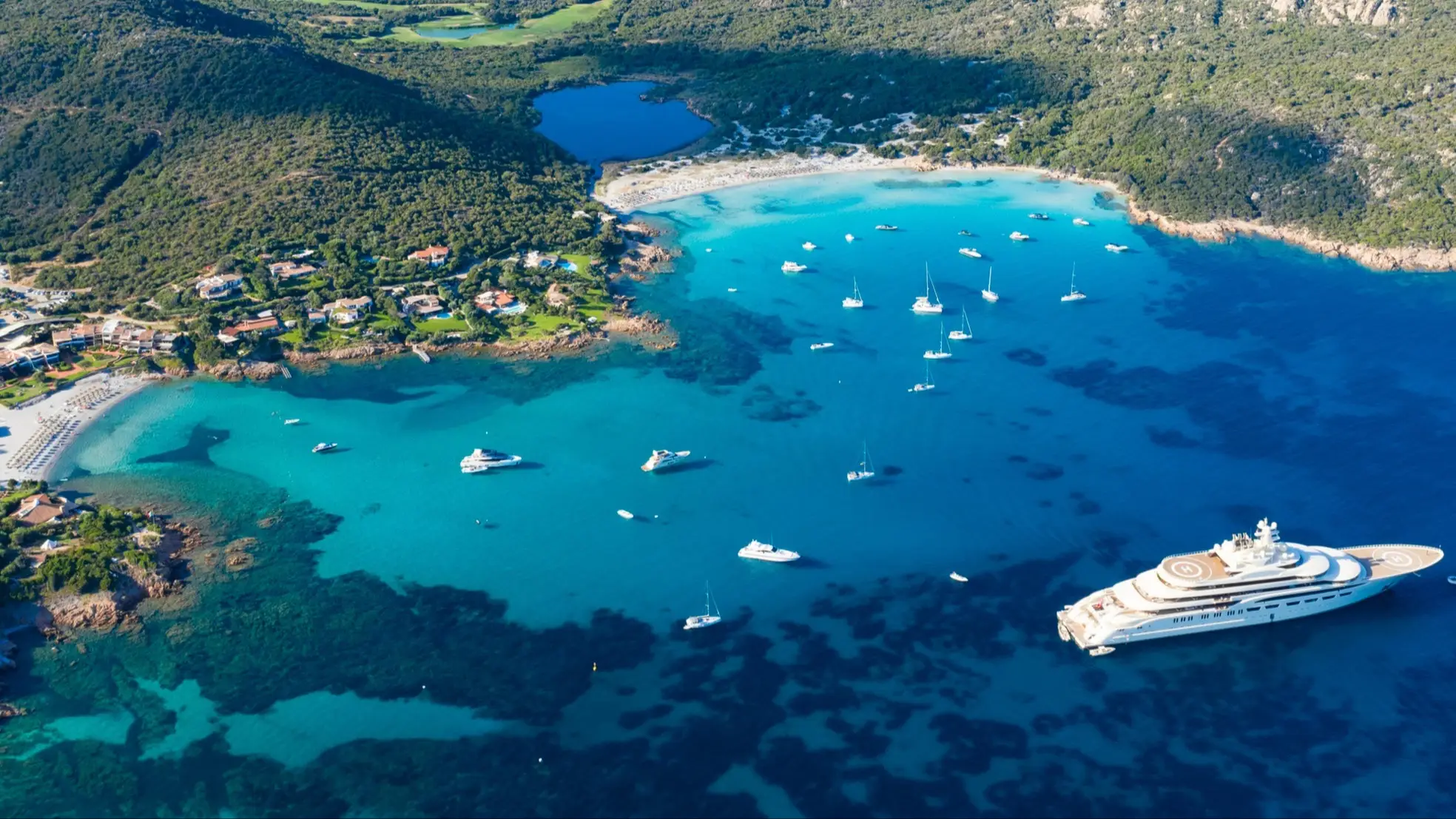 Italien, Sardinien, Grande Pevero Luftaufnahme des Strandes Grande Pevero, Sardinien, Italien mit Blick auf die grüne Küste, Häuser und Booten im Meer.