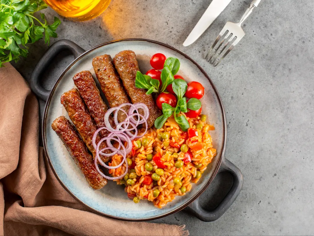 Ćevapčići, gegrillte Fleischröllchen mit typisch zubereiteten Reis und Beilagen.