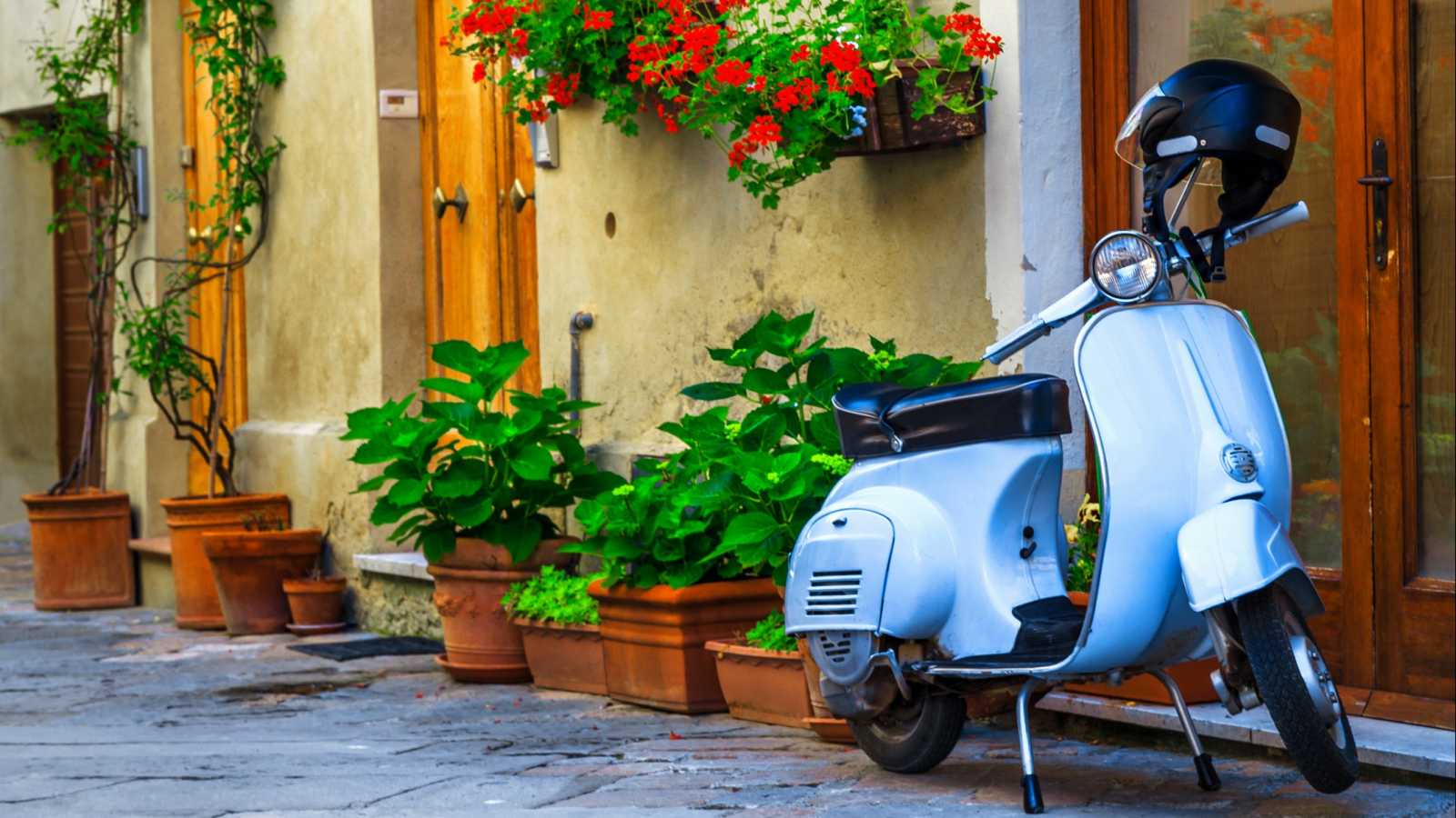 Wunderschöne, hübsch dekorierte Straße mit Blumen und rustikalem Eingang, altmodischer Motorroller in einer typischen italienischen Straße, Pienza, Toskana,