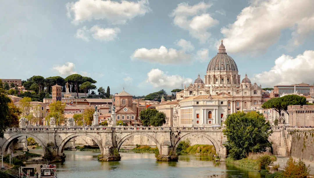 Panoramablick auf Rom mit Petersdom, historischer Brücke über den Tiber und blauem Himmel mit weißen Wolken.