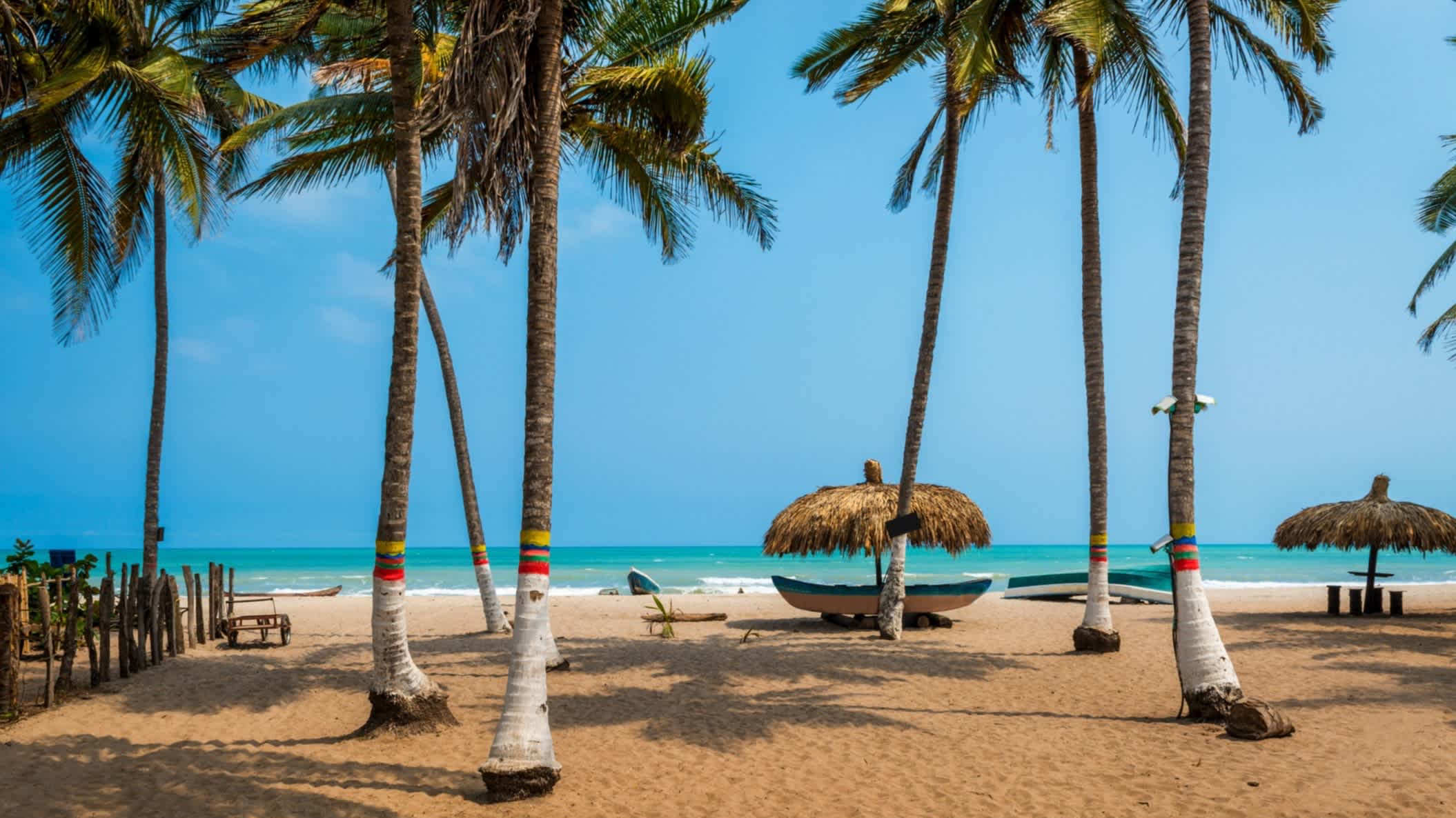 Der schöne Strand von Palomino an der Karibikküste von Kolumbien, Südamerika mit Palmen, Sonnenschirmen und dem Meer im Bild.