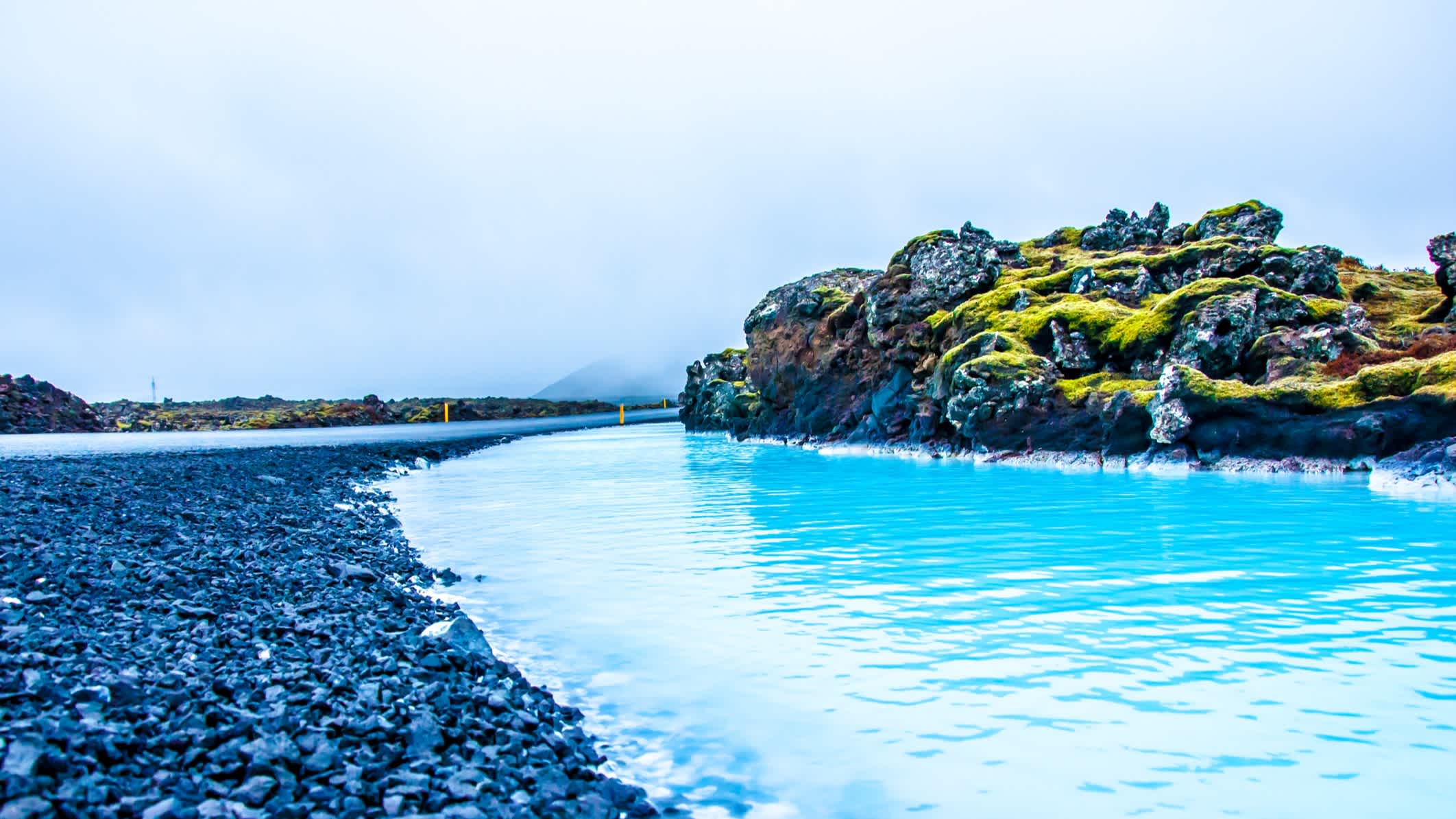 Die Blaue Lagune in Island mit schwarzem Kieselstrand und mossbewachsenen Steinen
