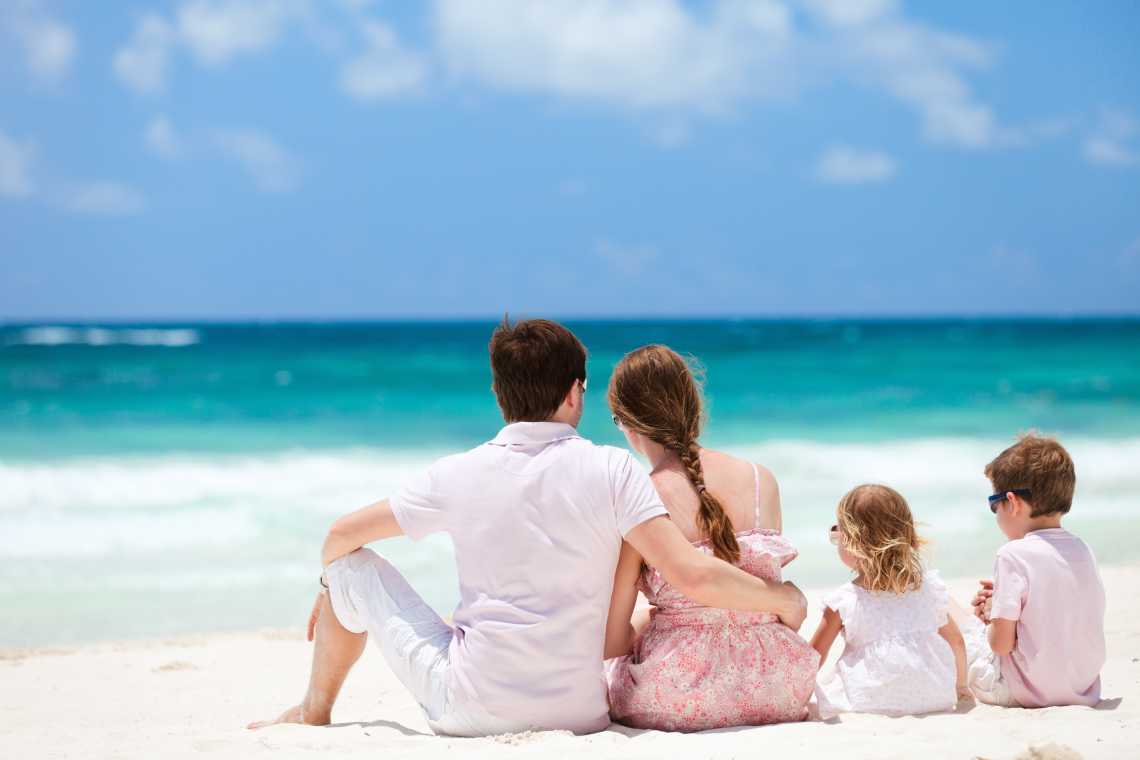 Une famille assise sur le sable face à l'océan, lors d'un voyage en famille au Mexique. 