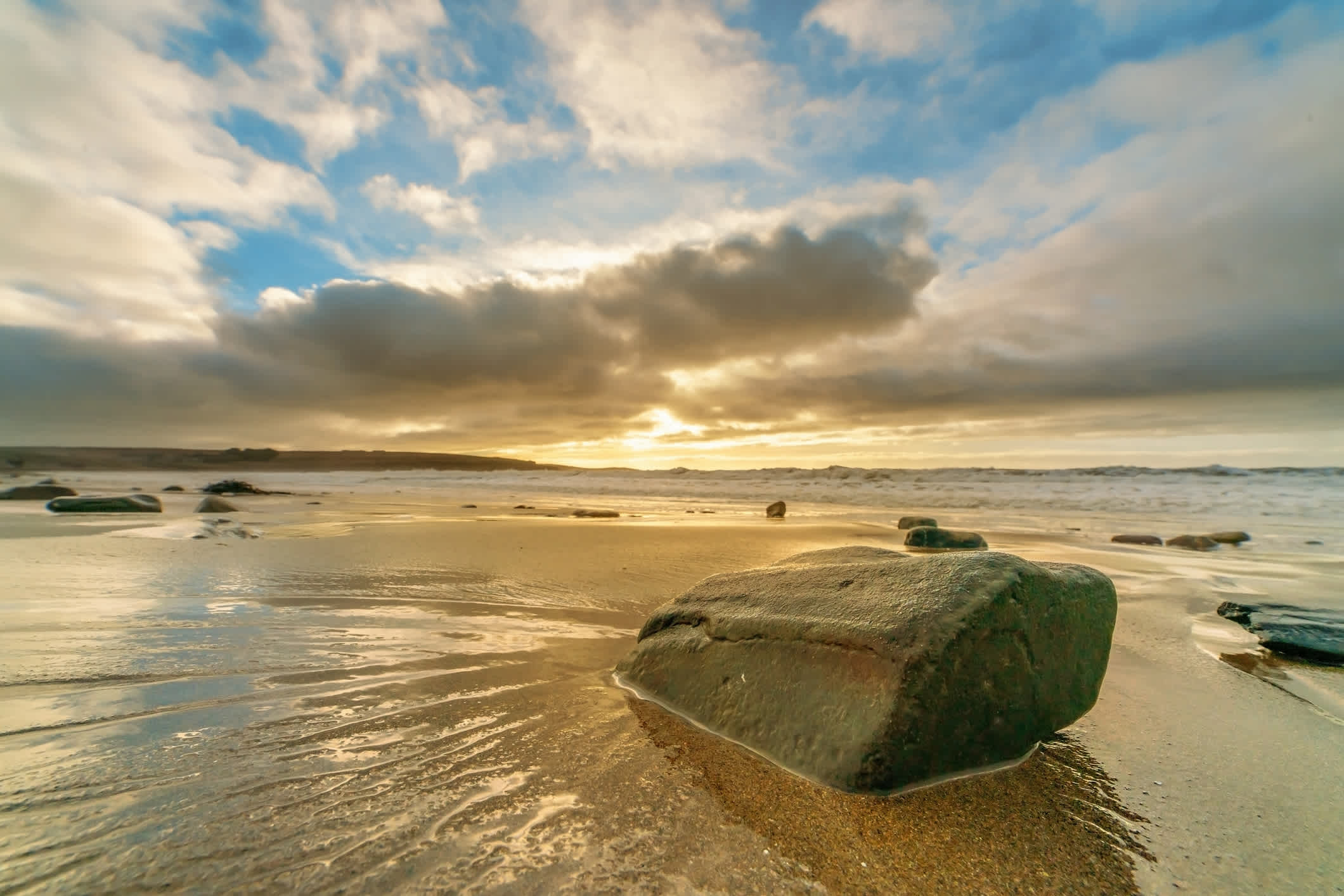 Rocher dans l'eau sur le sable au coucher de soleil sur une plage plate en Irlande