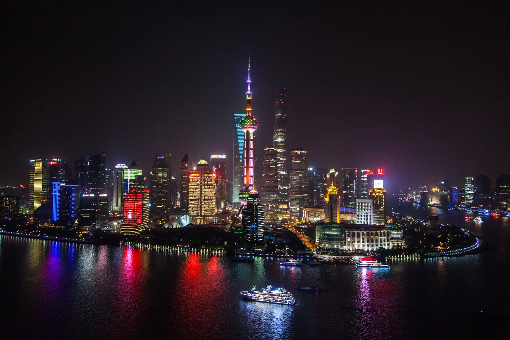 Nächtliche Skyline von Shanghai mit beleuchtetem Oriental Pearl Tower und Wolkenkratzern, die sich im Fluss Huangpu spiegeln.