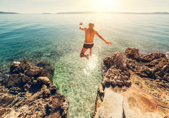 Homme en train de sauter d'une falaise dans une lagune bleu turquoise pendant des vacances en Croatie.