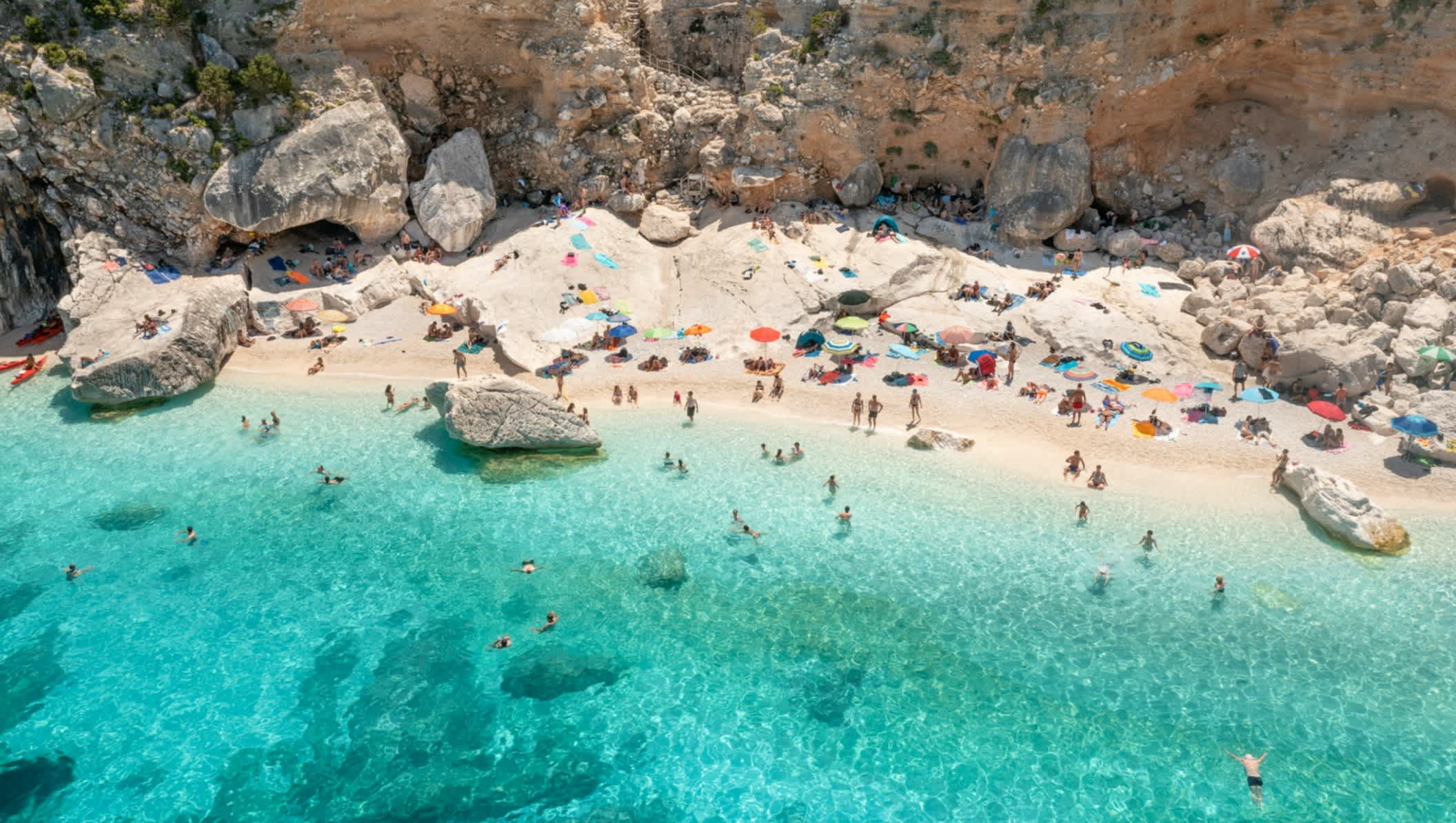 Personnes sur le sable clair et dans l'eau cristalline de la plage de Cala Goloritze en Italie 