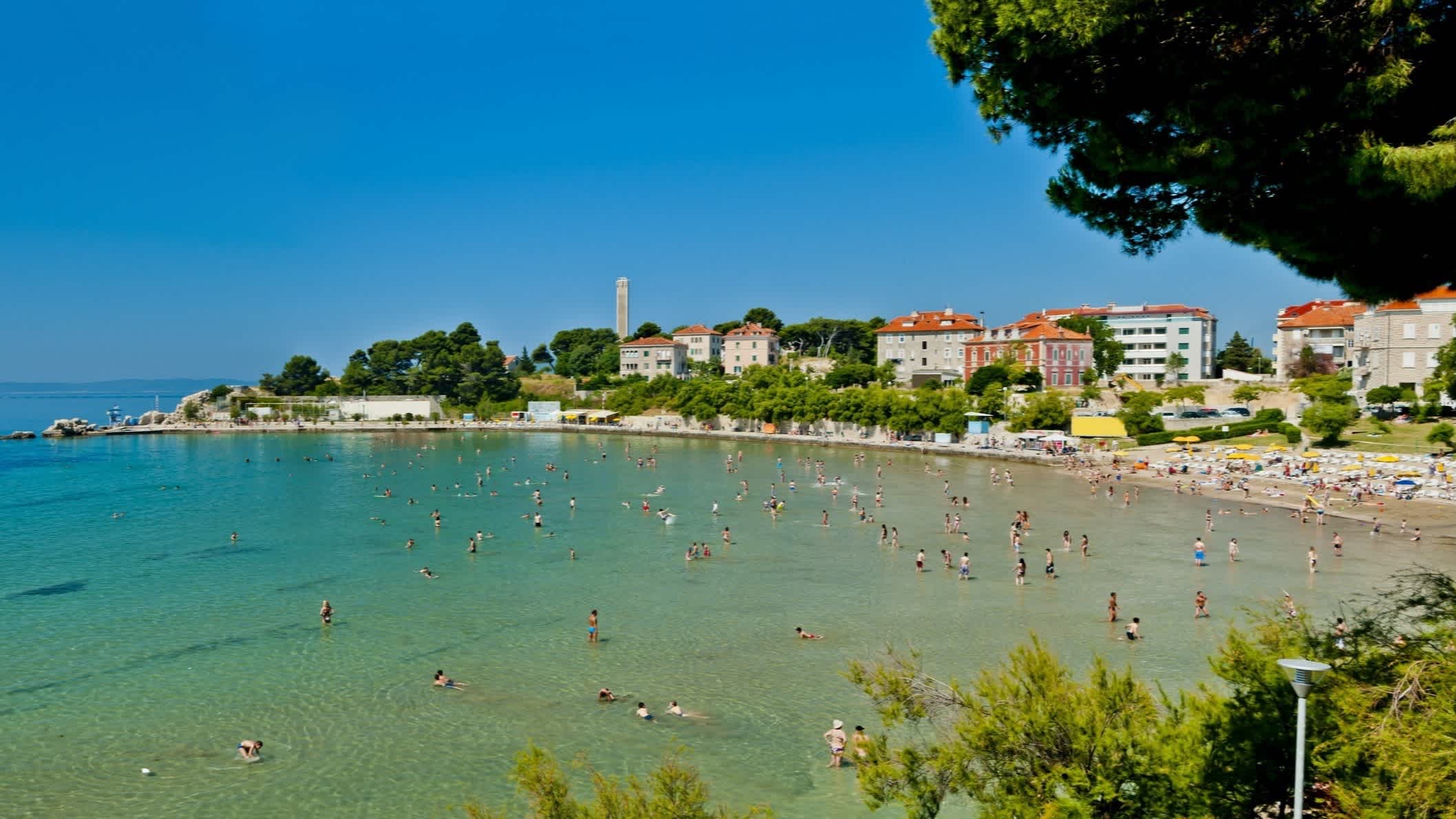Der Strand von Bačvice, Split, Kroatien mit Blick auf die mit Menschen gefüllte Bucht sowie Häusern im Bild.