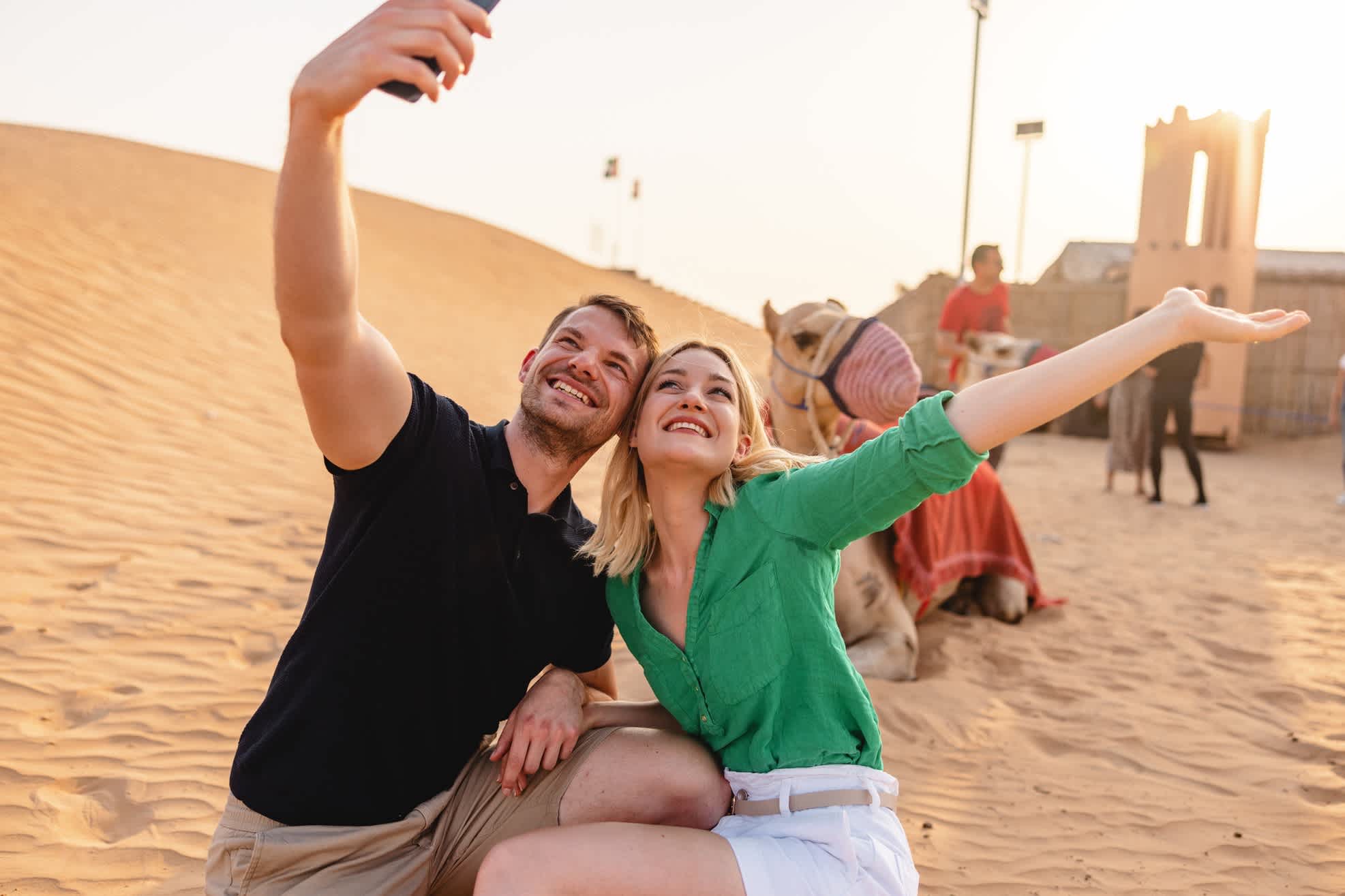 Ein Paar posiert vor einem Kamel in der Wüste und macht ein Selfie