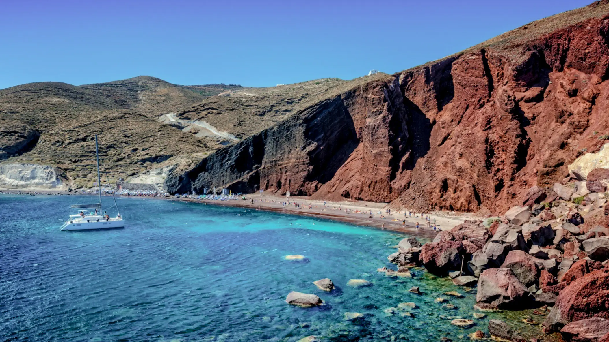 Griechenland, Santorini, Kamari Roter Vulkanstrand Kamari auf Santorini, Griechenland mit azurblauem Meer und einem Boot im Wasser.