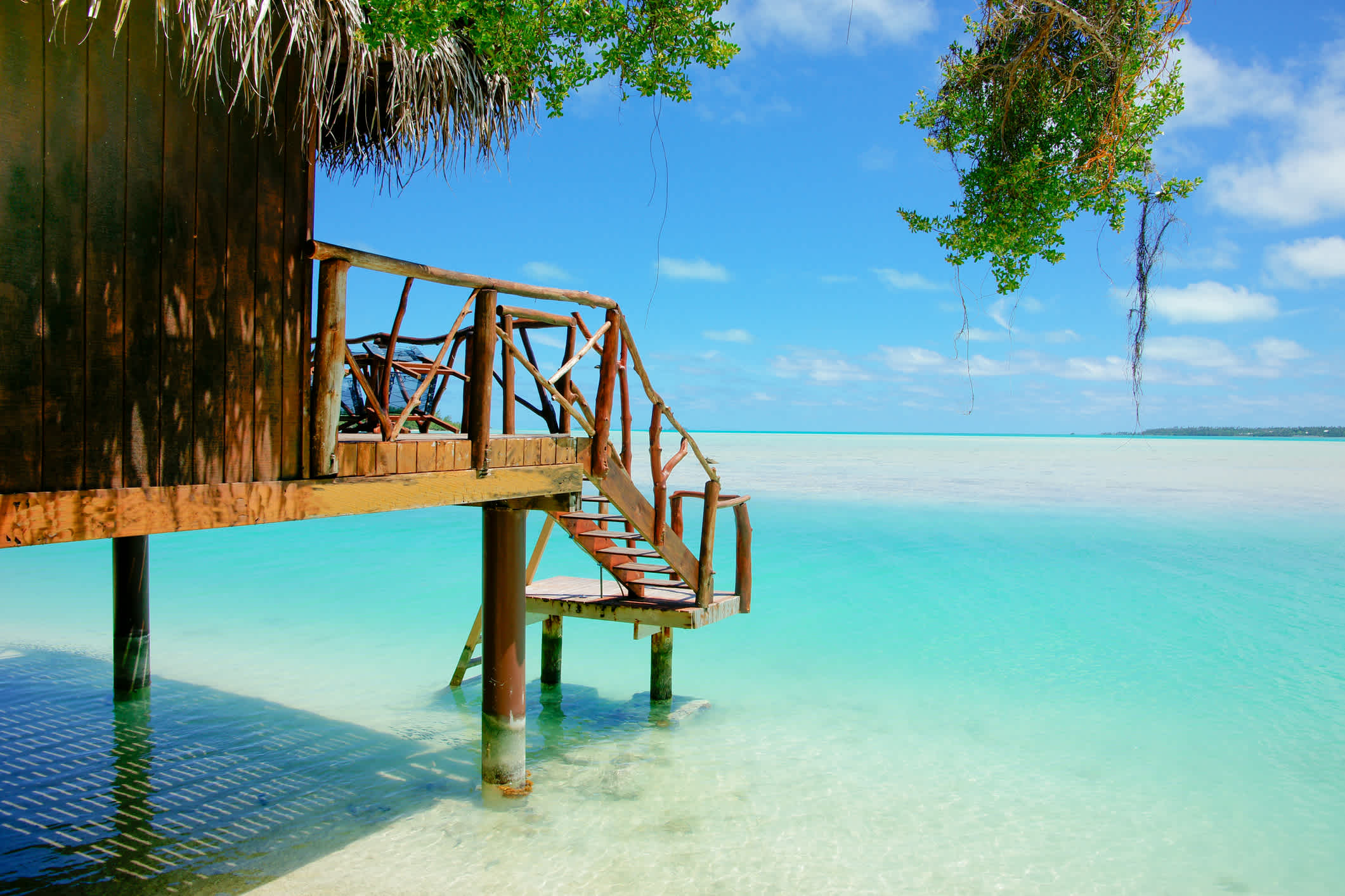 Stufen hinunter zu einem Holzsteg über dem Wasser auf einer tropischen Insel mit Blick auf den Horizont über türkisfarbenem Wasser.