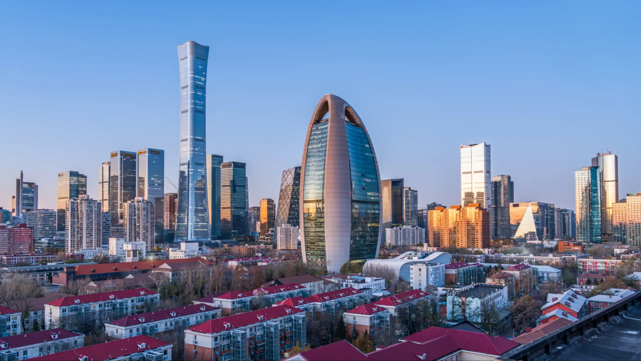Skyline von Peking mit dem markanten eiförmigen CITIC-Tower und Wolkenkratzern über Wohngebieten mit roten Dächern.