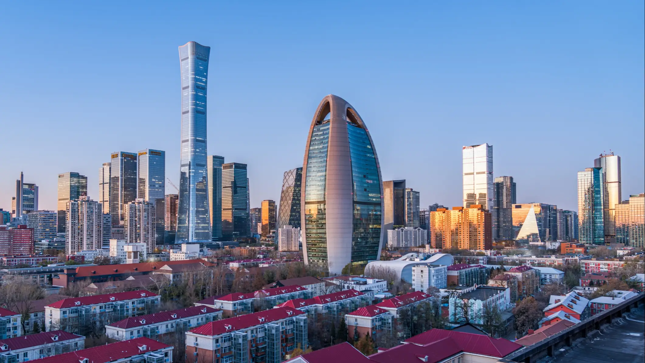 Skyline von Peking mit dem markanten eiförmigen CITIC-Tower und Wolkenkratzern über Wohngebieten mit roten Dächern.
