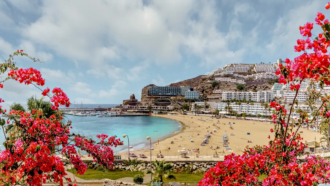 Strand mit Blumen, blauen Wasser und Hotels. Puerto Rico, Gran Canaria, Spanien.
