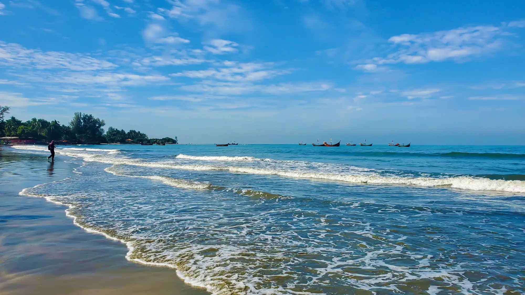 Cherating Beach, Pahang, Malaisie Plage tropicale avec eau turquoise, vagues douces, bateaux de pêche à l'horizon et ciel bleu parsemé de nuages blancs, Malaisie.