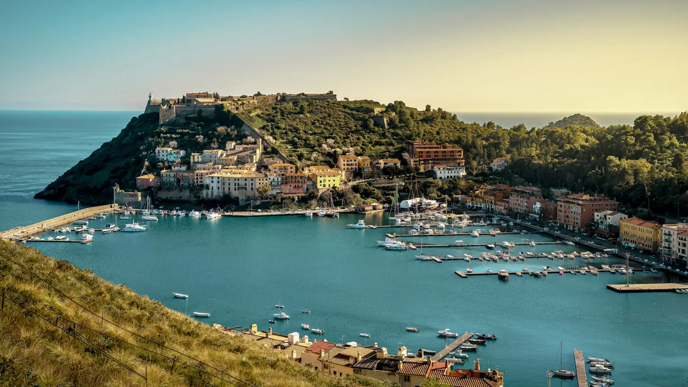 Harbor with colorful houses and green peninsula. Monte Argentario, Tuscany, Italy.