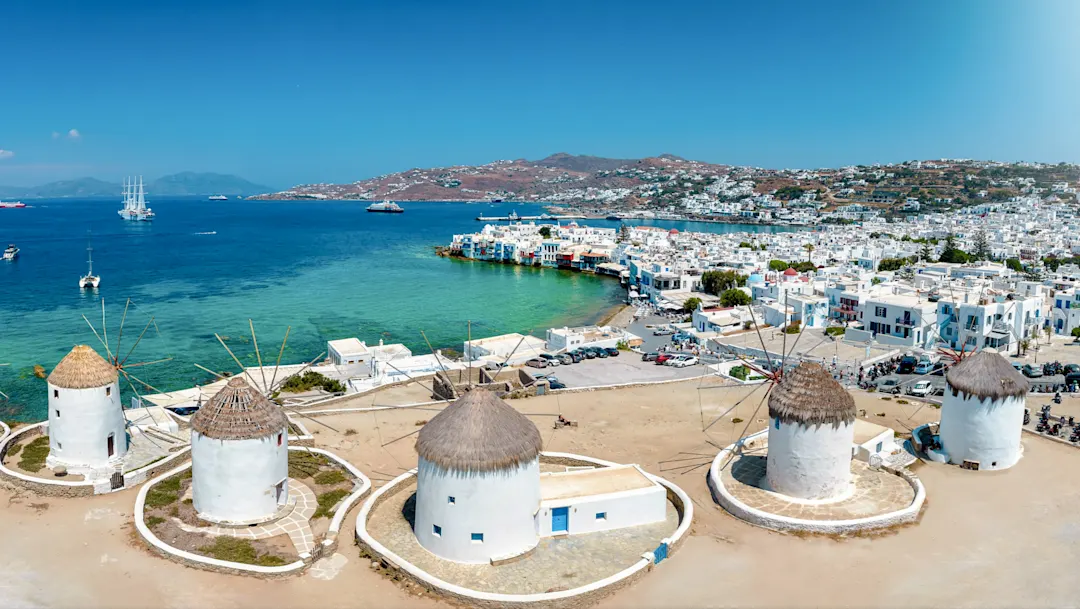 Traditionelle Windmühlen mit Blick auf das blaue Meer und die Stadt im Hintergrund. Mykonos, Kykladen, Griechenland.