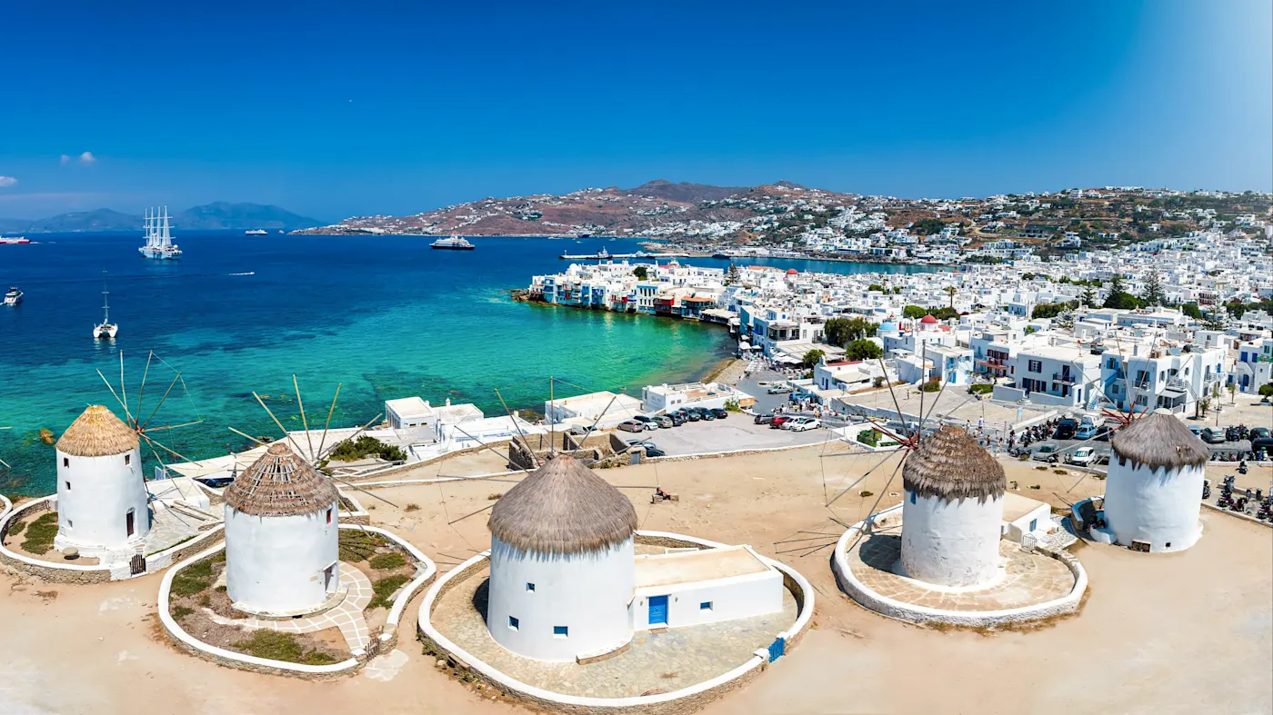 Griechenland, Mykonos, Kykladen, Windmühlen Traditionelle Windmühlen mit Blick auf das blaue Meer und die Stadt im Hintergrund. Mykonos, Kykladen, Griechenland.