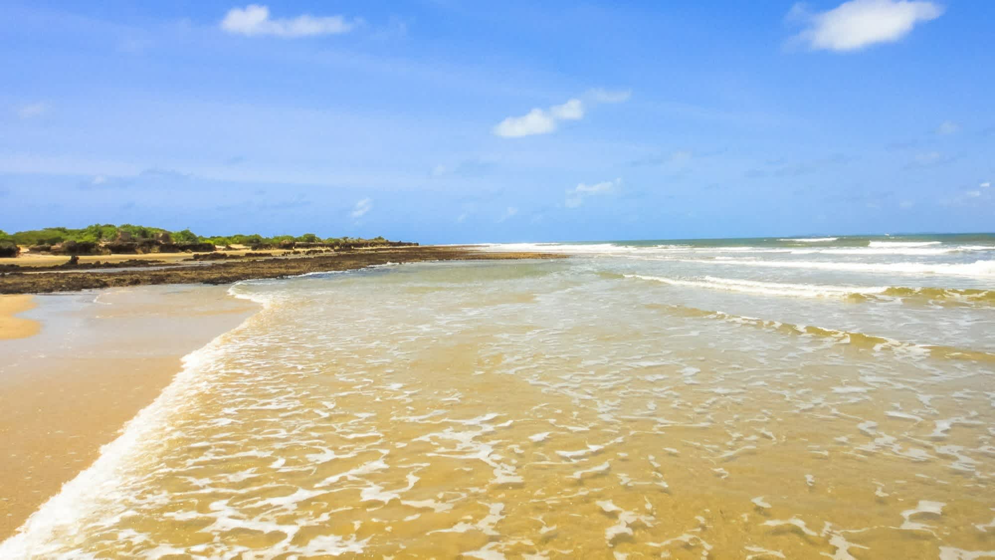 Blick auf den goldenen Sandstrand Manda Beach in Kenia mit Wellen und natürlichem Ambiente.