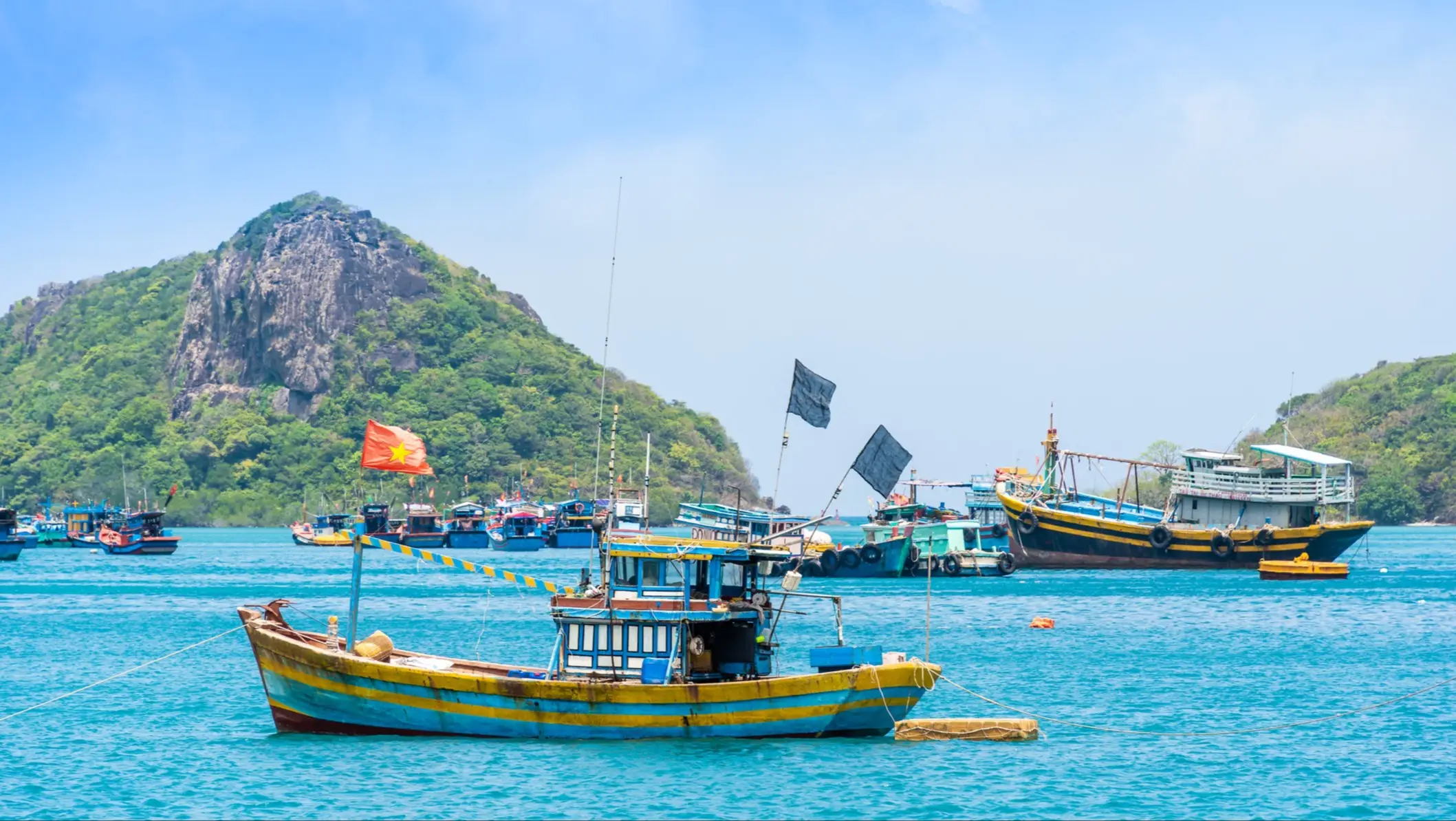 Le port de Ben Dam, sur l'île de Con Dao, au Vietnam, avec sa mer bleue, son ciel bleu, ses montagnes et ses bateaux colorés.