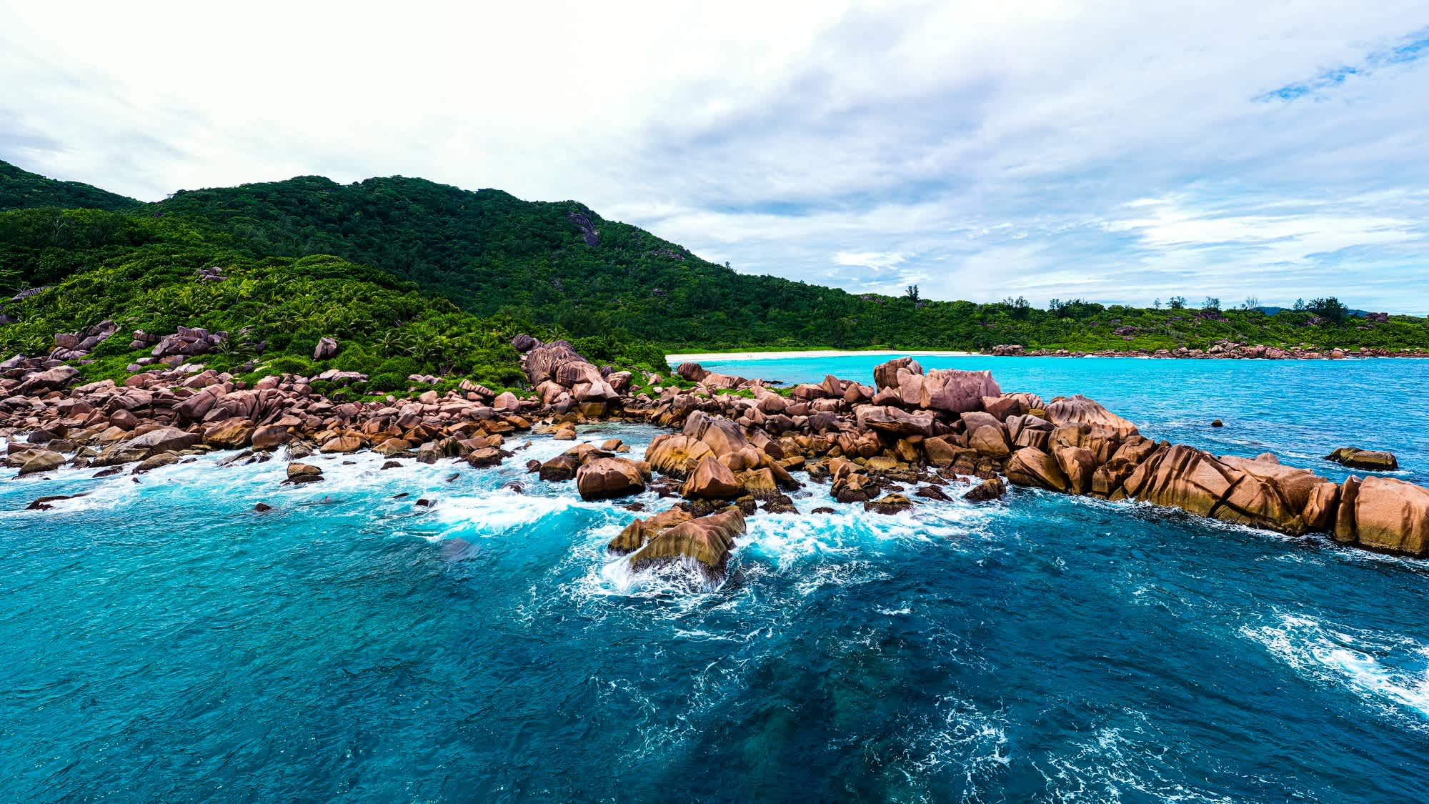 Drohnenaufnahme von der privaten North Island mit Blick auf die Granitfelsen, das Meer sowie die üppige Vegetation und den Strand auf den Seychellen.