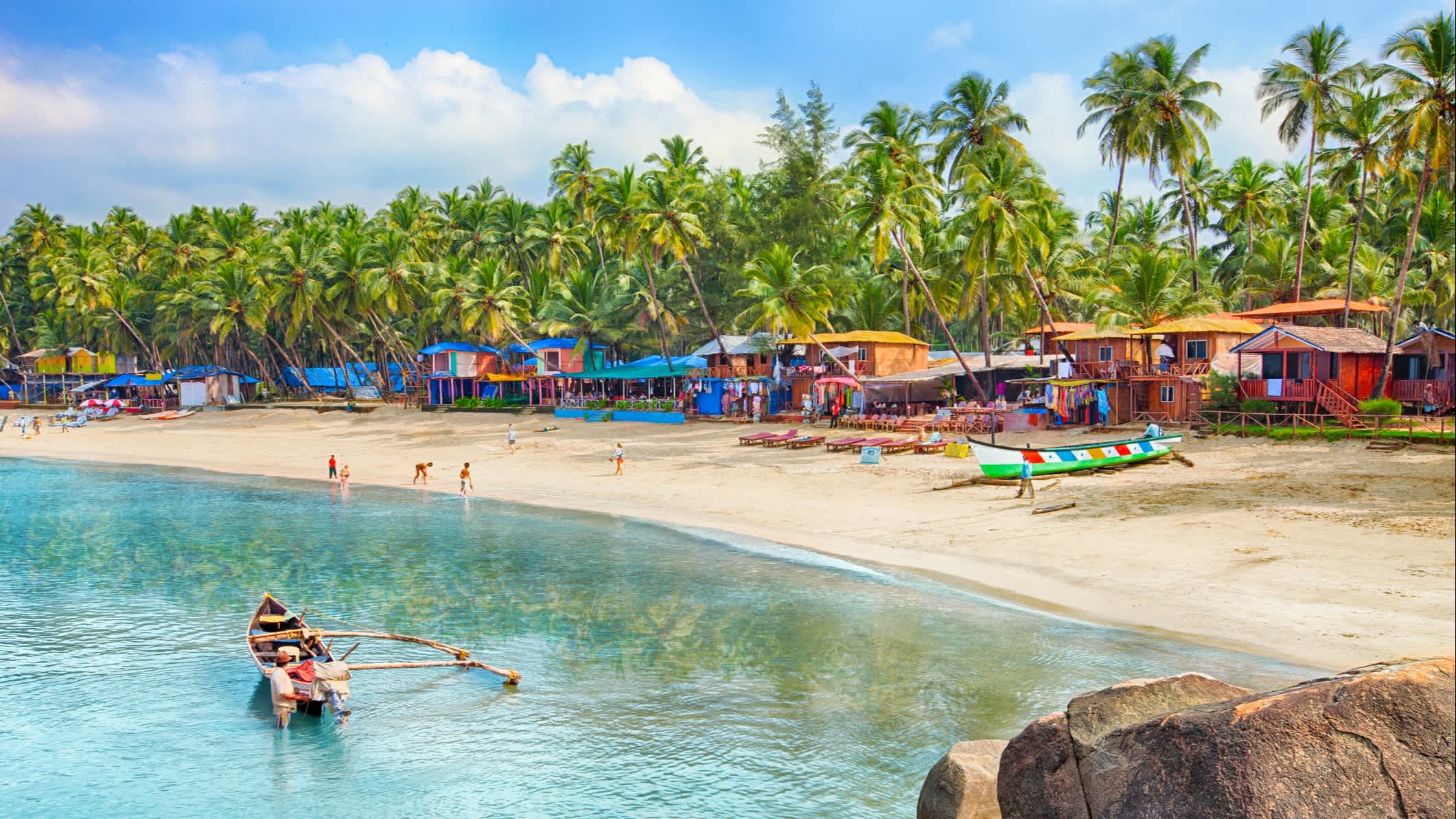 Bateau sur l'eau au bord d'une plage bordé de maisons colorées parmi les palmiers, à Goa, en Inde