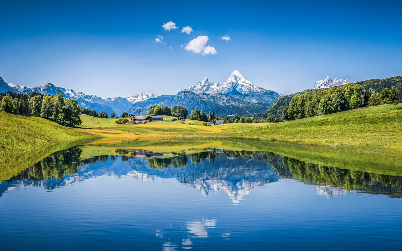 Lake, Alps, mountains, Switzerland Snow-capped mountains reflected in a calm lake surrounded by green meadows and forests under a bright blue sky.