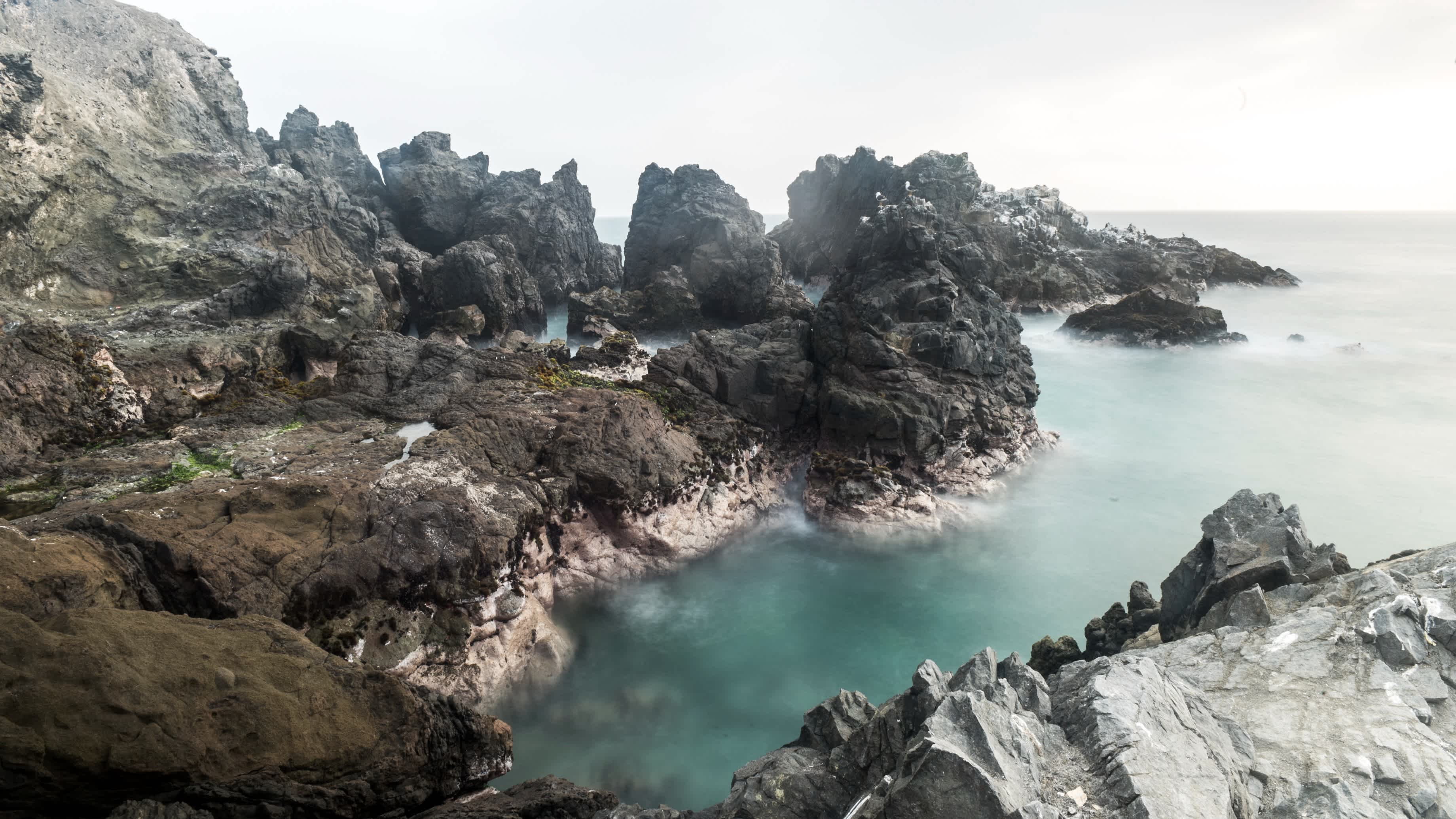 Die Bucht von San Bartolo nahe Lima, Peru bei bewölktem Wetter mit schroffen Felsen sowie türkisem Wasser.