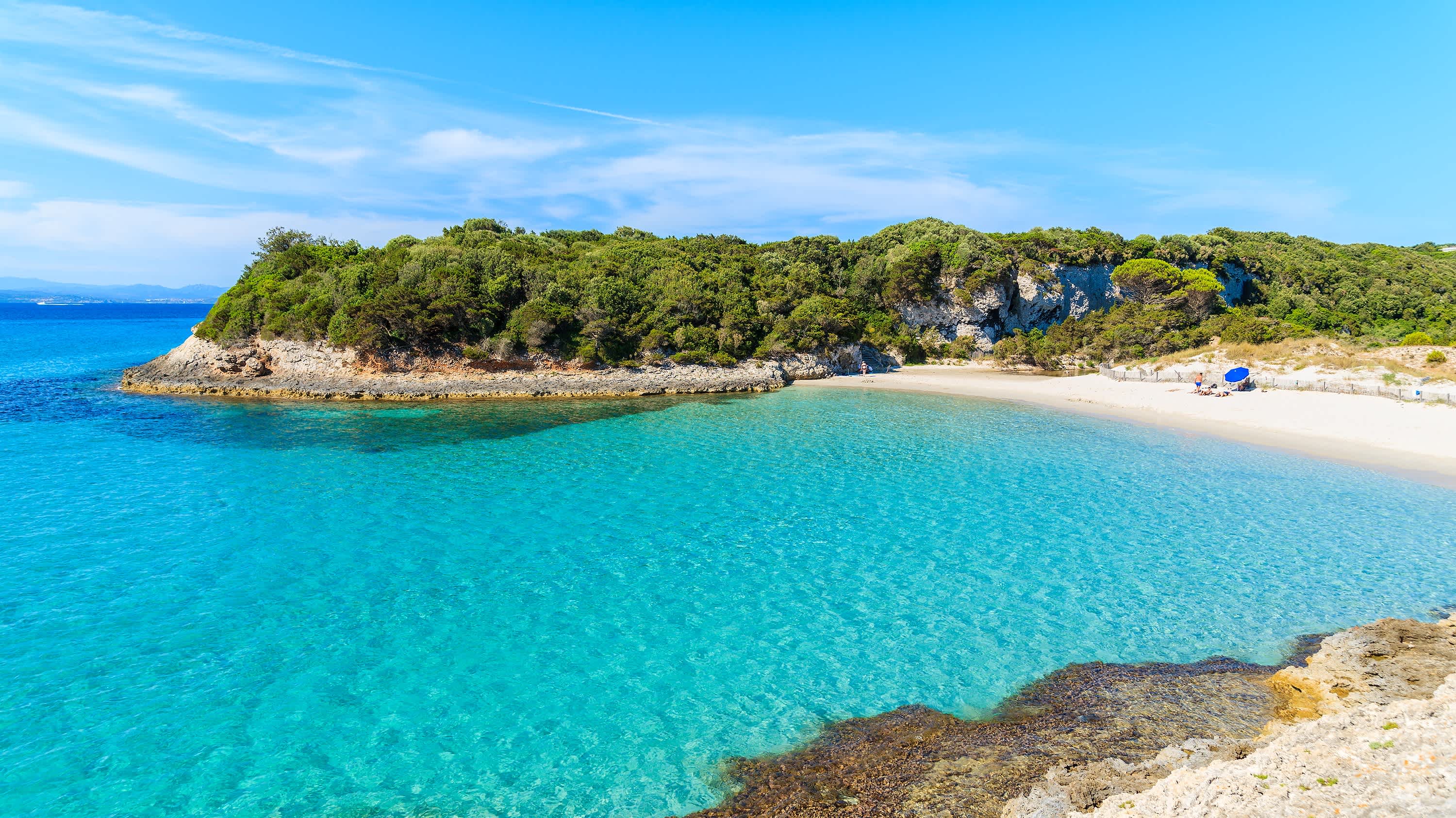 Vue de l'eau turquoise et du sable blanc entourés de rochers verdoyants sur la plage du Petit Sperone en Corse, France
