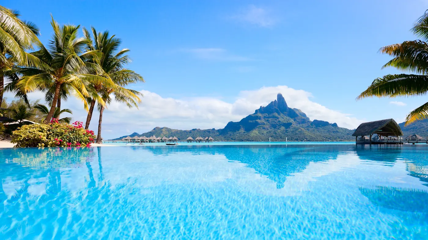 Polynésie Française, Bora bora, piscine Piscine à débordement avec vue sur Bora Bora, palmiers et bungalows sur pilotis sous un ciel bleu éclatant.