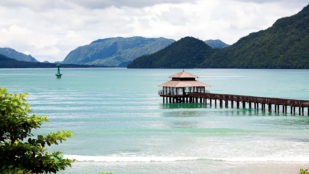 Holzsteg über türkisfarbenem Wasser mit Hügeln im Hintergrund. Langkawi, Kedah, Malaysia.