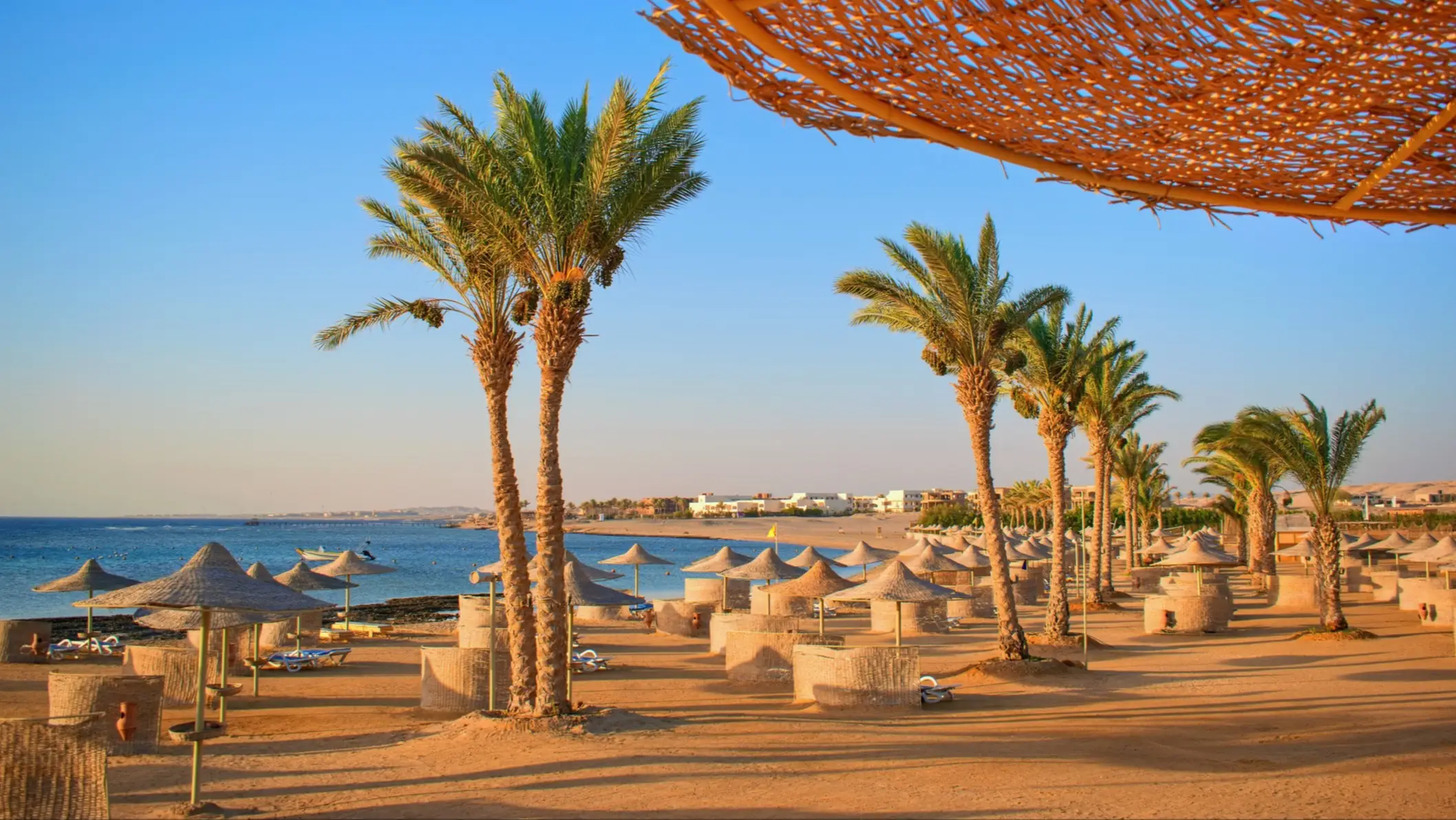 Plage avec palmiers et parasols de paille sur la mer Rouge au coucher du soleil. Hurghada, mer Rouge, Égypte.