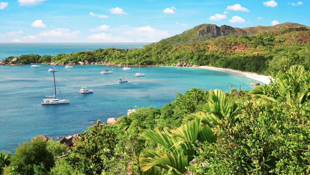 Segelboote in türkisblauem Wasser mit grüner Landschaft. Anse Lazio, Praslin, Seychellen.