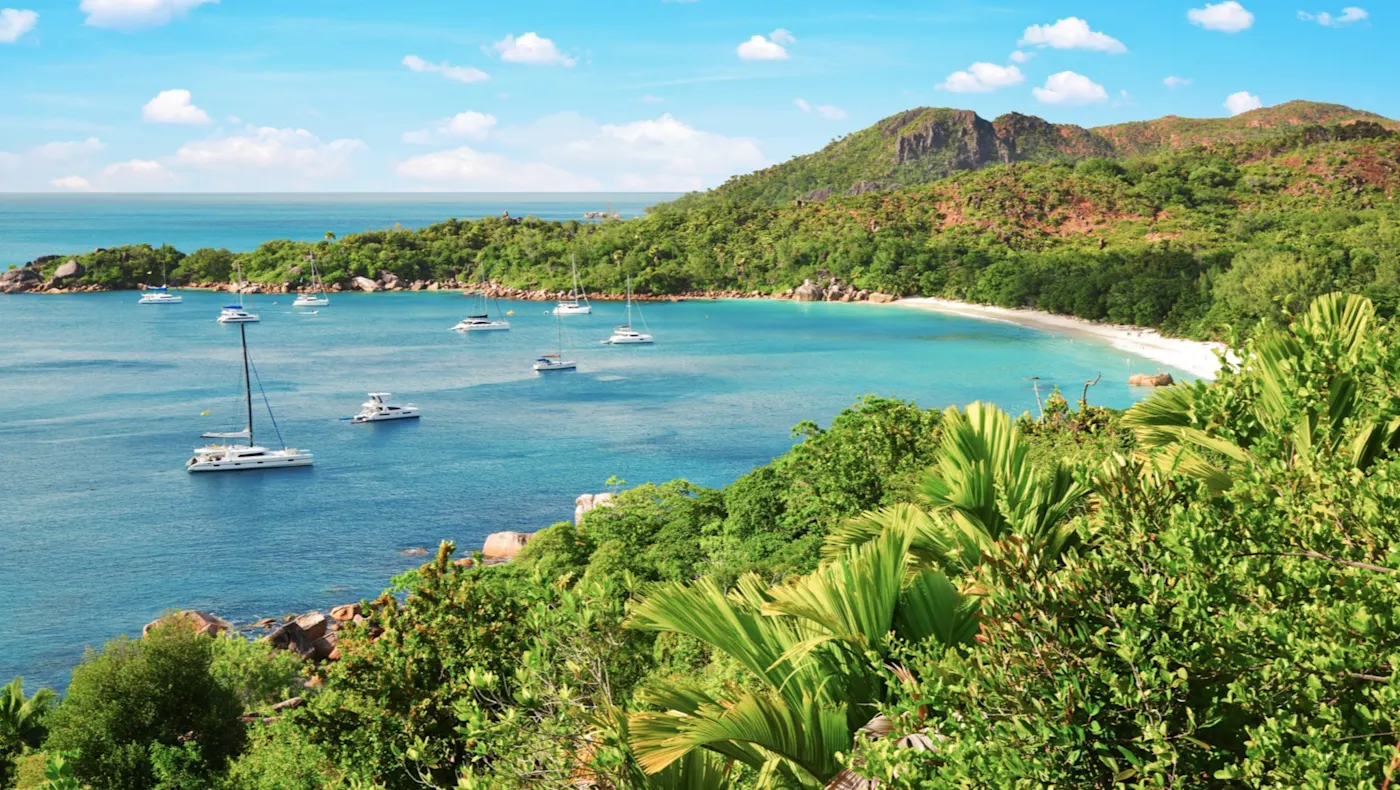 Segelboote in türkisblauem Wasser mit grüner Landschaft. Anse Lazio, Praslin, Seychellen.