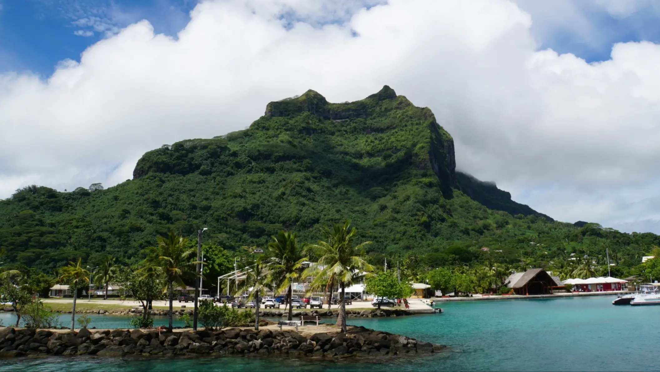 Montagne de Otemanu surplombant le port de Vaitape, avec palmiers et eaux turquoise, Polynésie Française.