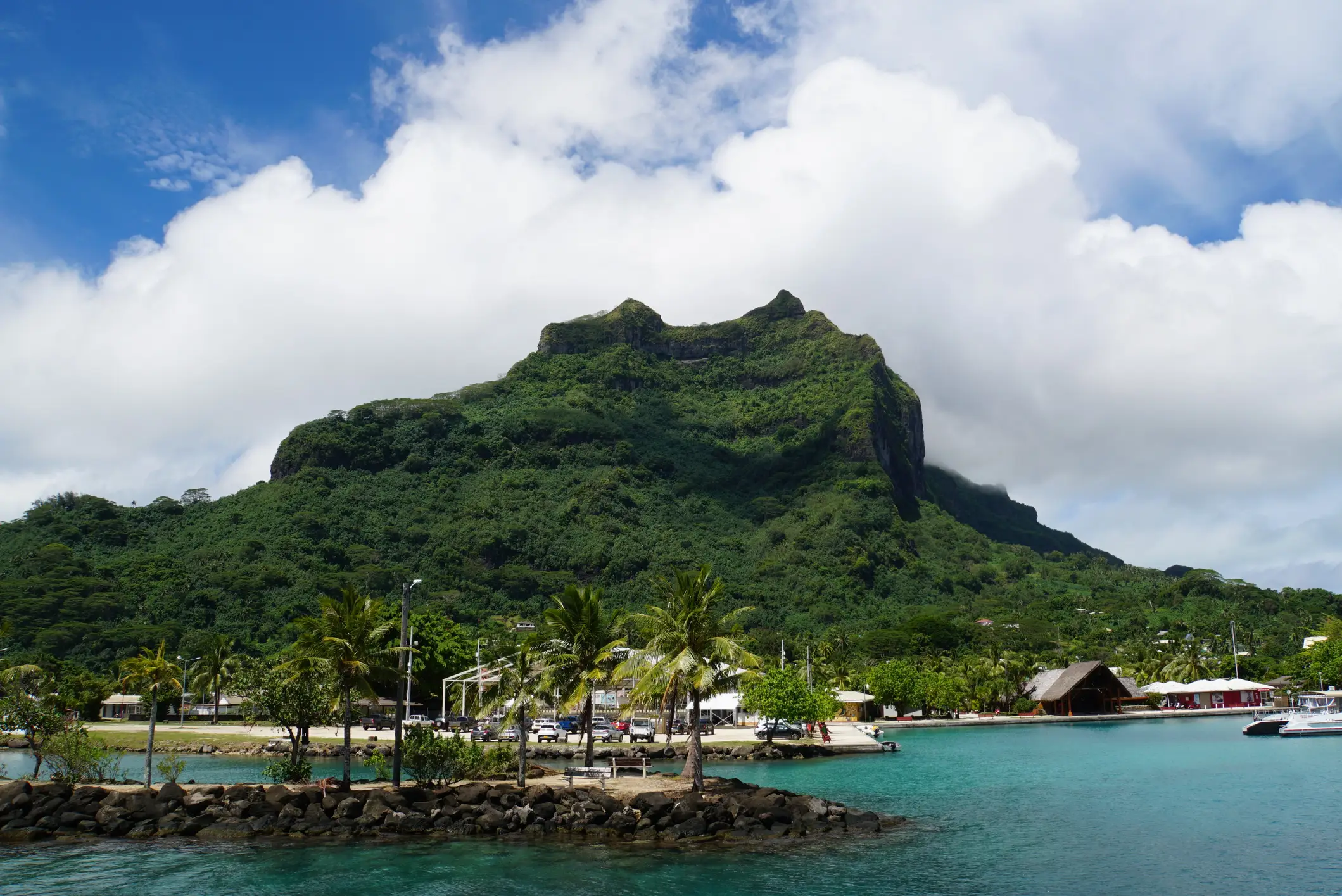 Montagne de Otemanu surplombant le port de Vaitape, avec palmiers et eaux turquoise, Polynésie Française.