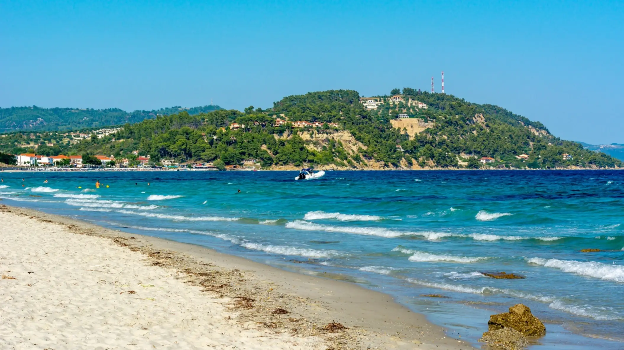 Griechenland, Chalkidiki, Posidi Strand Der Posidi Strand auf der Halbinsel Kassandra, Chalkidiki, Griechenland bei sonnigem Wetter, mit Wellen im Wasser sowie Bergen im Hintergrund.