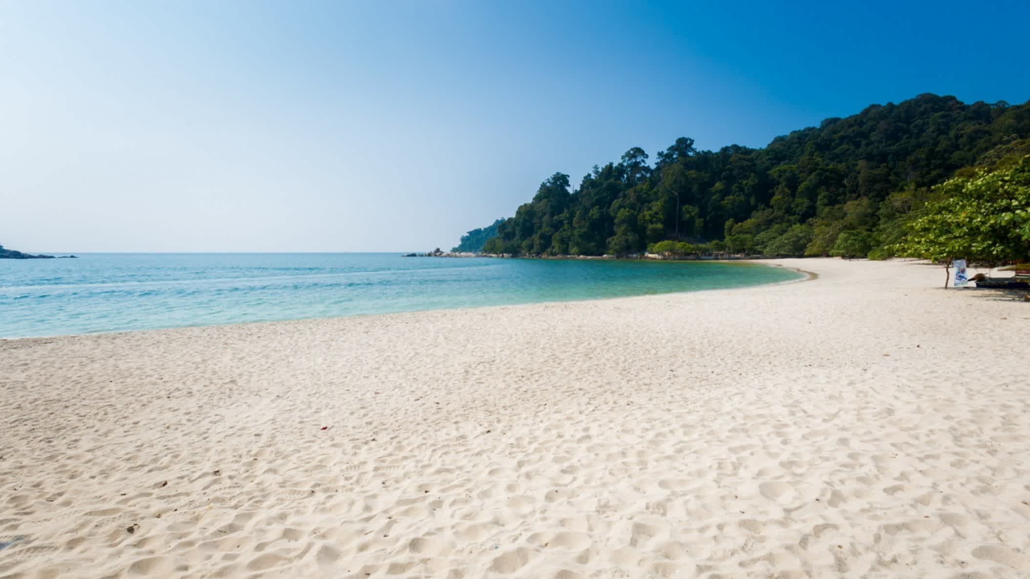 Der Strand Teluk Nipah Coral Strand, Pangkor, Malaysia mit weißem Sand und grüner Vegetation im Hintergrund.