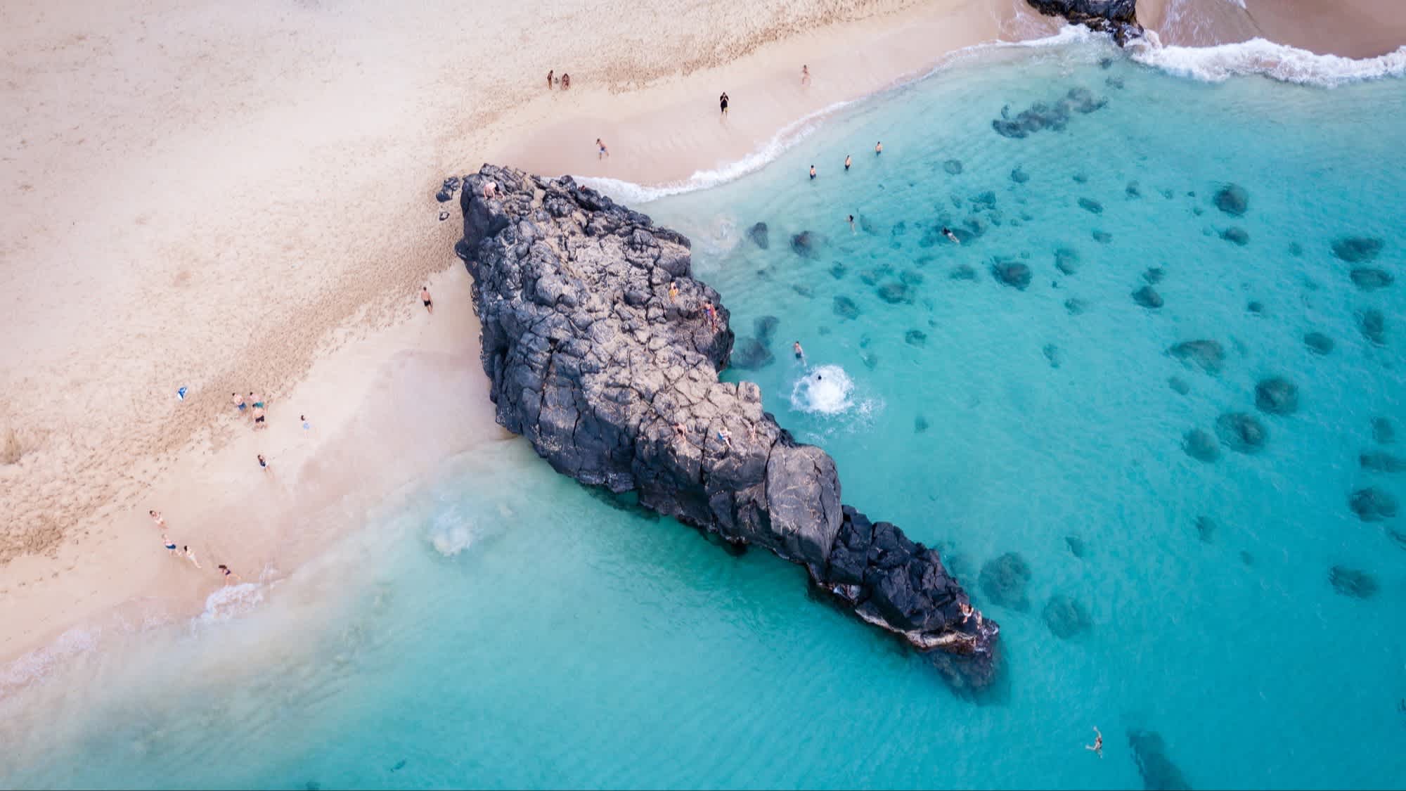 Der Strand Waimea Bay, Oahu, Hawaii, USA bei Sonnenschein und mit Blick auf das Meer aus der Luft sowie einer riesigen Felsansammlung.
