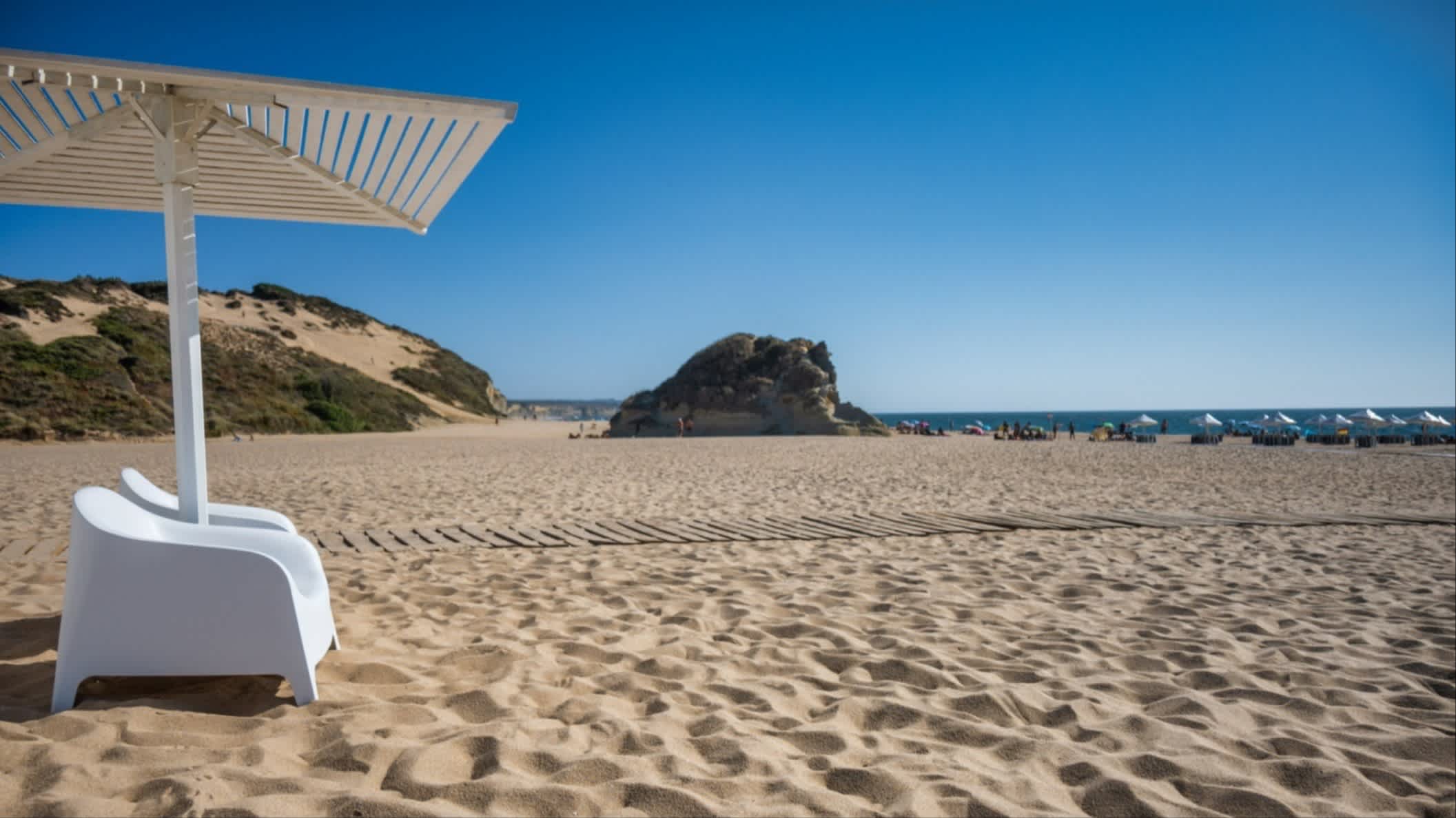 Ein Sonnenschirm und Sessel am Strand von Praia do Meco, Sesimbra, Portugal mit Meerblick und bei Sonnenschein.