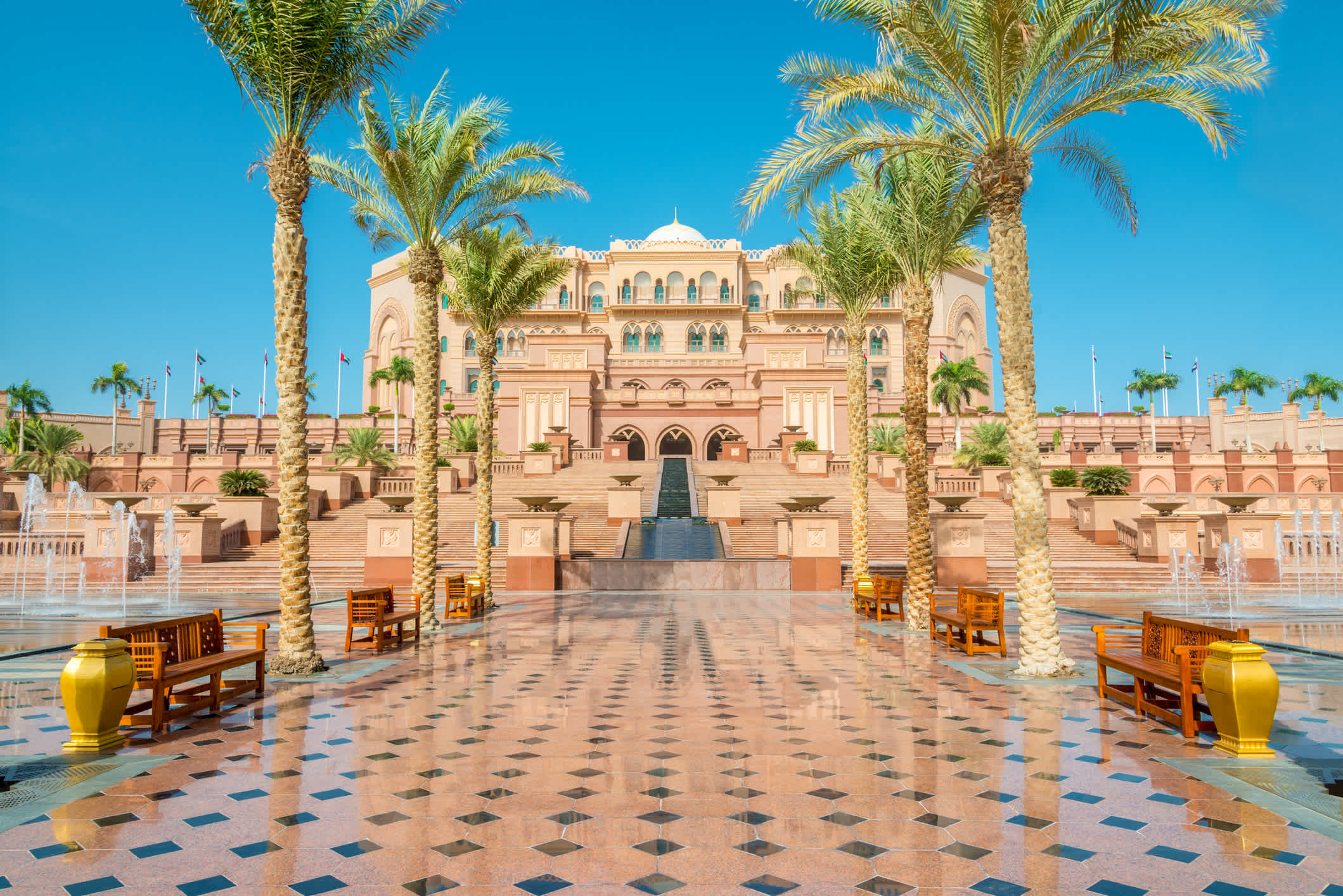 Vorplatz eines prunkvollen Gebäudes in arabischer Architektur, mit Palmen gesäumt.
