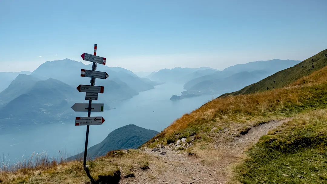 Wanderweg mit Wegweisern und Blick auf den Comer See in der Lombardei, Italien.