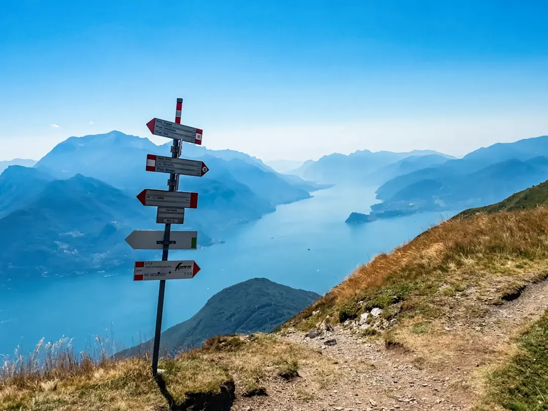 Wanderweg mit Wegweisern und Blick auf den Comer See in der Lombardei, Italien.