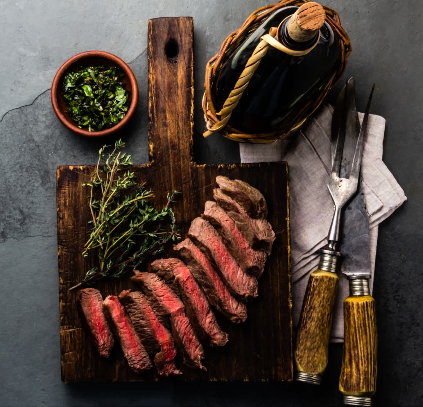 Steak de bœuf découpé et accompagné de vin et d'herbes aromatiques, posé sur une ardoise grise