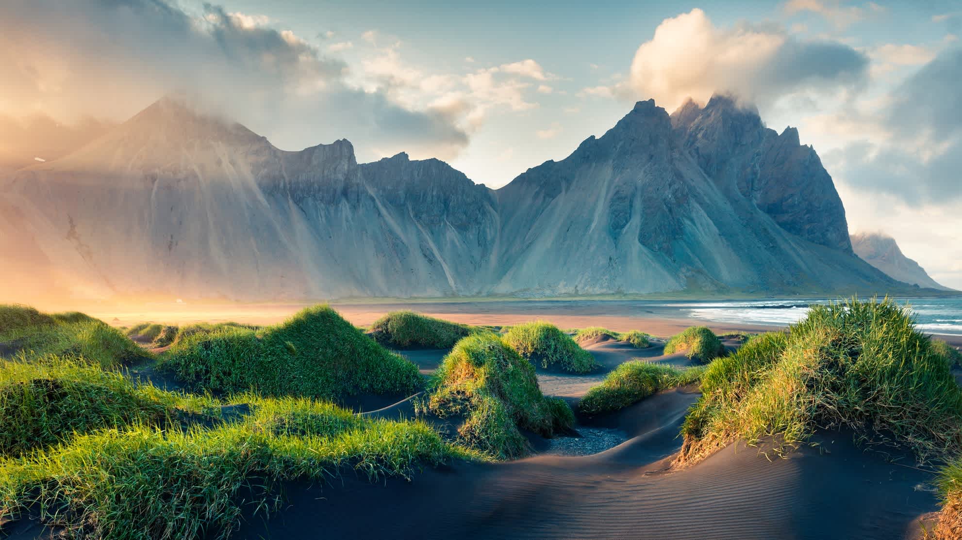 Schwarze Sanddünen auf der Landzunge Stokksnes in Island mit imposanten Bergen und dem Meer im Hintergrund. 