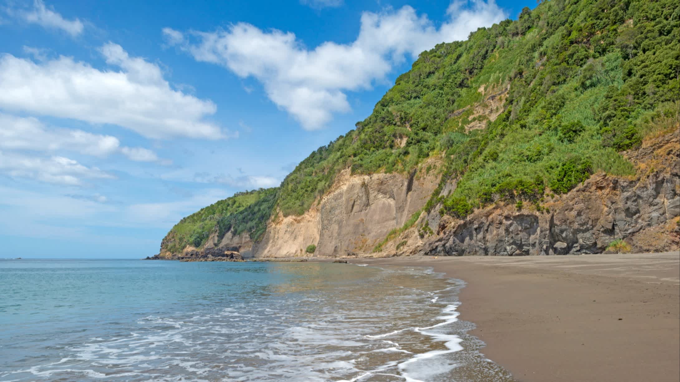 Vue sur le sable au bord de l'eau et des falaises verdoyantes sur la plage d'Agua de Alto sur l'île de São Miguel, aux Açores, au Portugal.