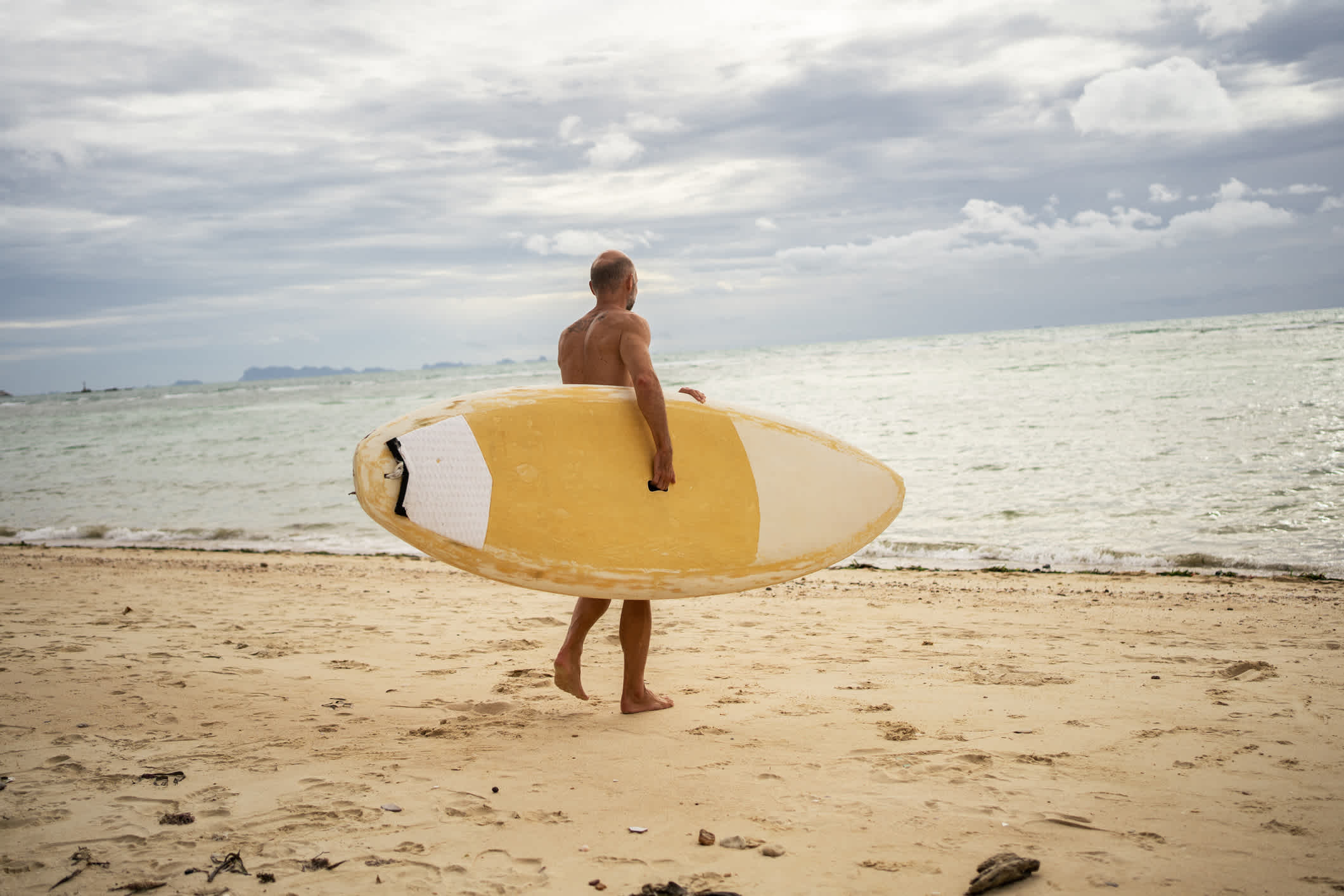 Un homme porte une planche à pagaie et se dirige vers la mer, Thaïlande